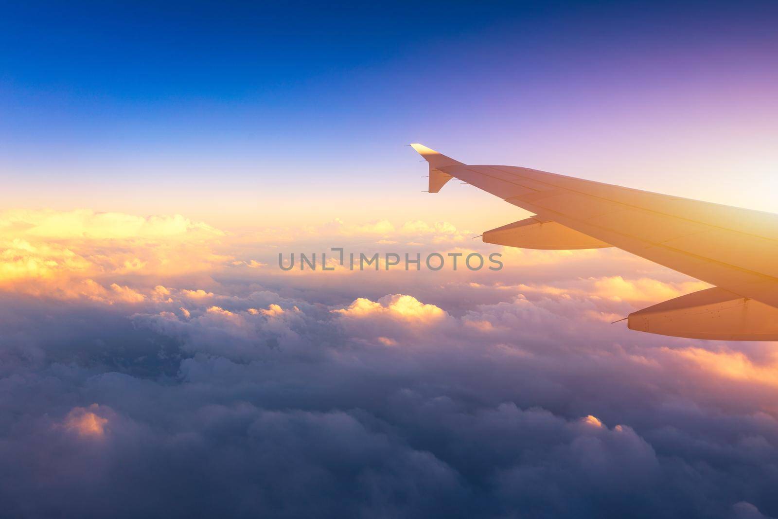 Flying and traveling, view from airplane window on the wing on sunset time. Aircraft wing under the earth and clouds. Flight in sky. Looking over aircraft wing in flight. 
