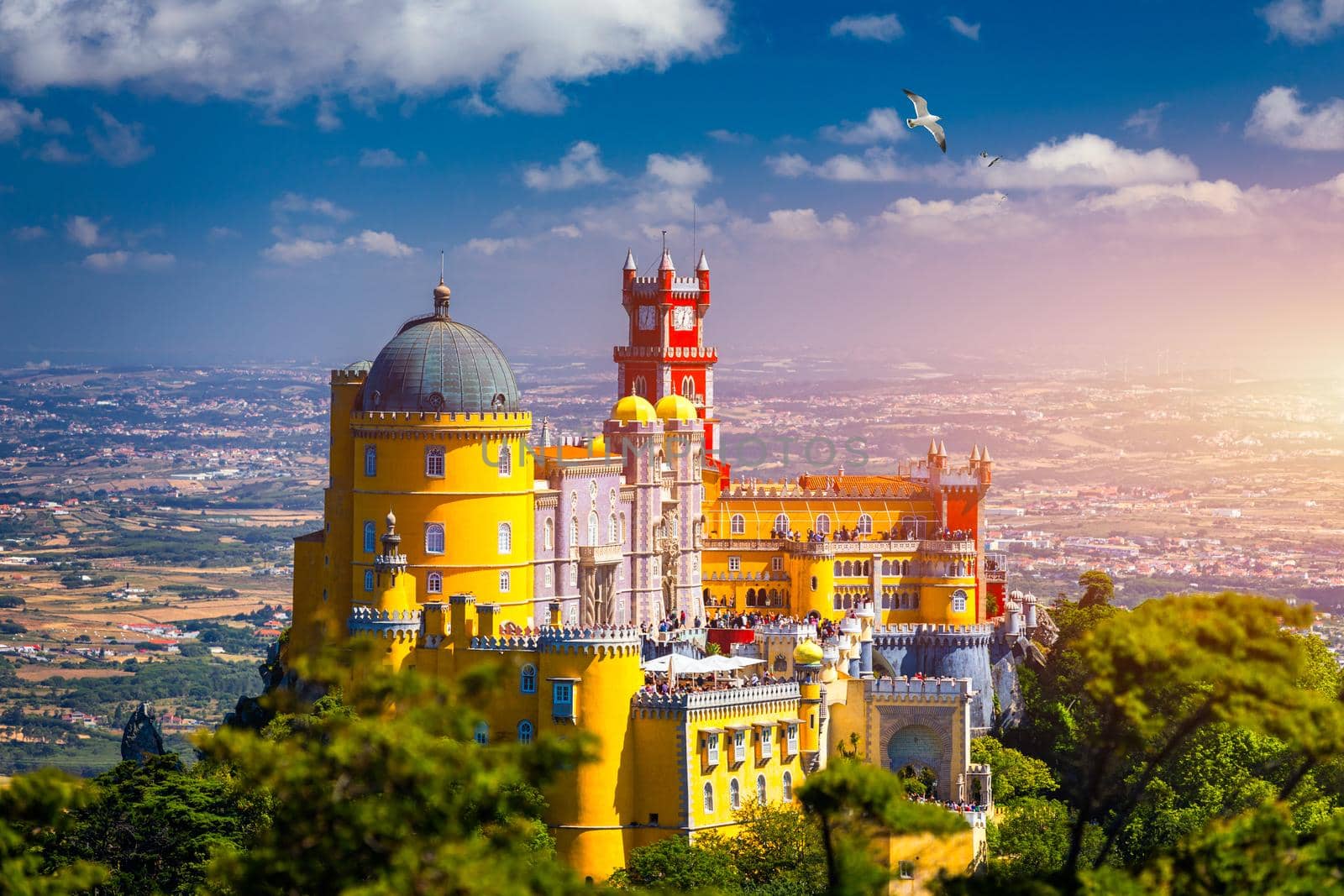 Famous historic Pena palace part of cultural site of Sintra against sunset sky in Portugal. Panoramic View Of Pena Palace, Sintra, Portugal. Pena National Palace at sunset, Sintra, Portugal. 
