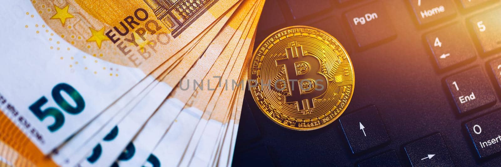 Golden bitcoin over Euro money. Bitcoin cryptocurrency. Crypto currency concept. Bitcoin with euro bills. Bitcoins stacked on euro banknotes. Computer keyboard used as background.