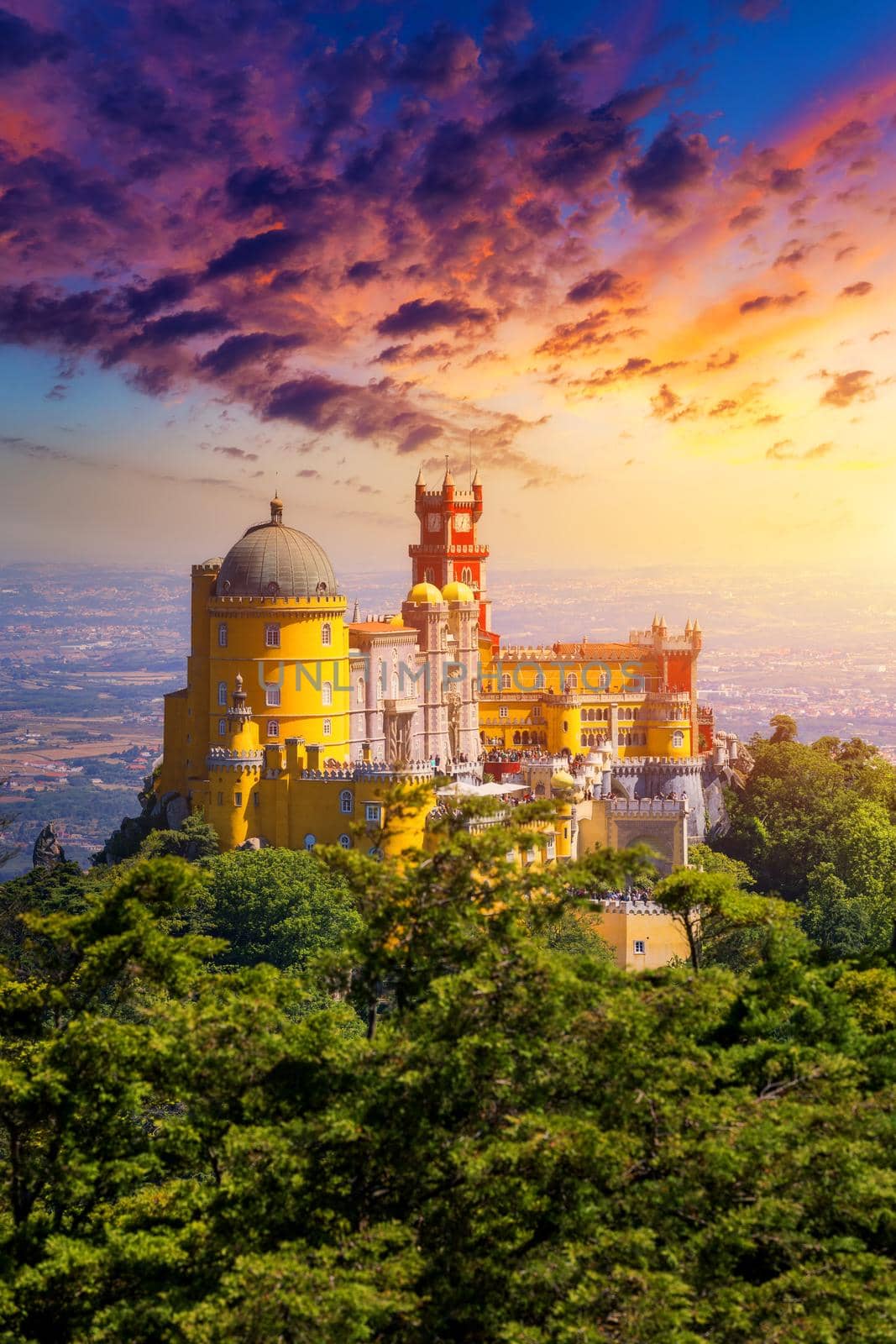 Famous historic Pena palace part of cultural site of Sintra against sunset sky in Portugal. Panoramic View Of Pena Palace, Sintra, Portugal. Pena National Palace at sunset, Sintra, Portugal. 