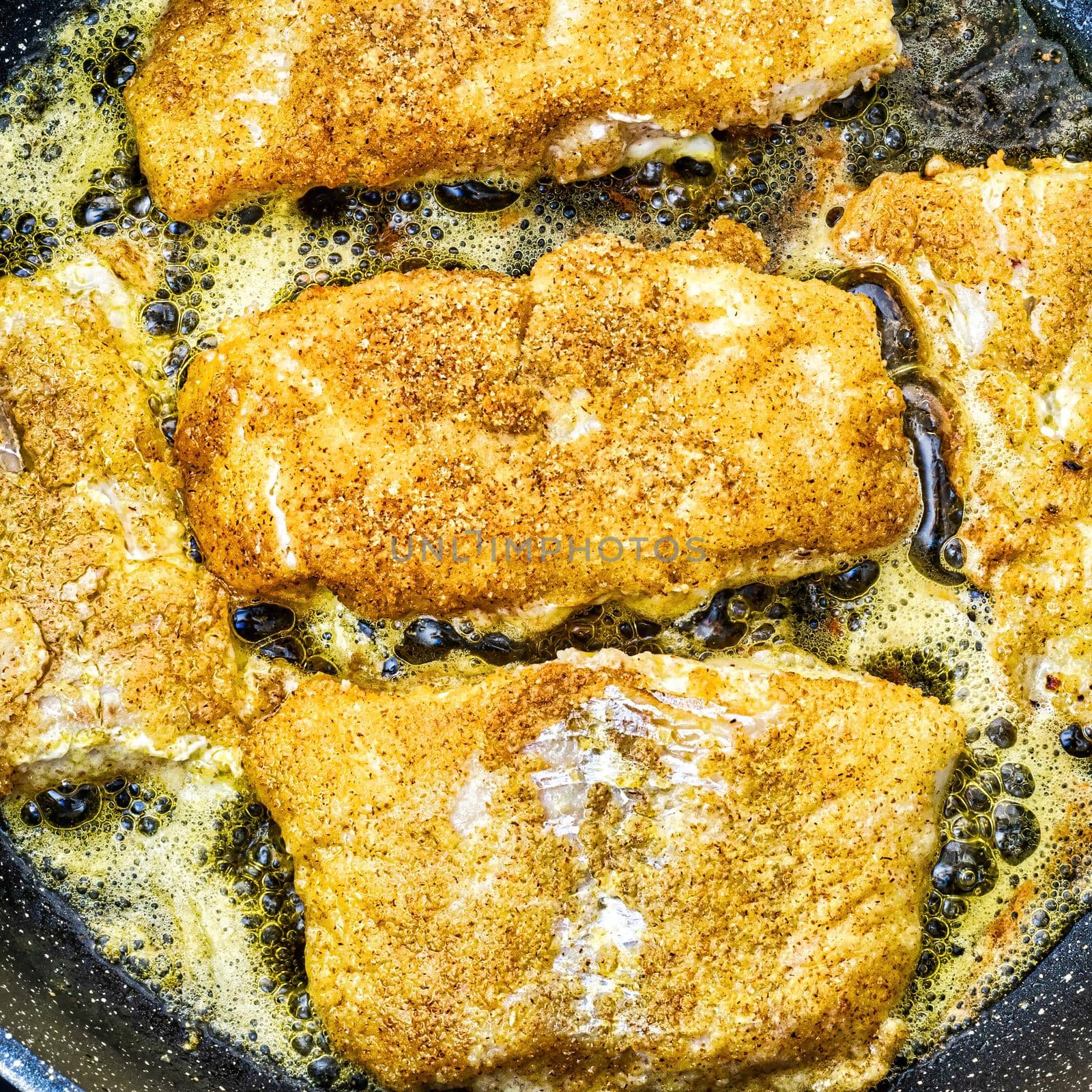 Breaded white fish steaks, fried in a pan with vegetable oil.