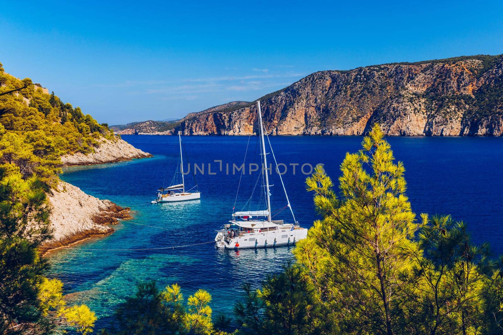Yacht anchoring in crystal clear turquoise water in front of the tropical island, alternative lifestyle, living on a boat. Aerial view of yacht at anchor on turquoise water, showing luxury, wealth.