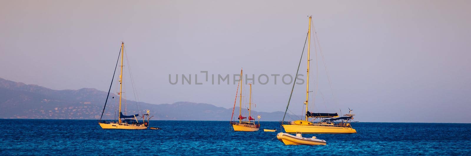 Yacht anchoring in crystal clear turquoise water in front of the tropical island, alternative lifestyle, living on a boat. Aerial view of yacht at anchor on turquoise water, showing luxury, wealth.