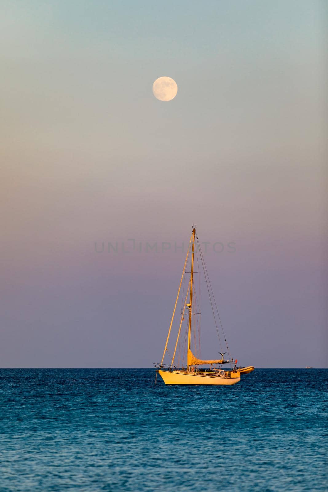 Aerial view of anchored sailing yacht in emerald sea. Aerial view of a boat. Outdoor water sports, yachting. Aerial view of anchoring yacht in open water. Ocean and sea travel and transportation