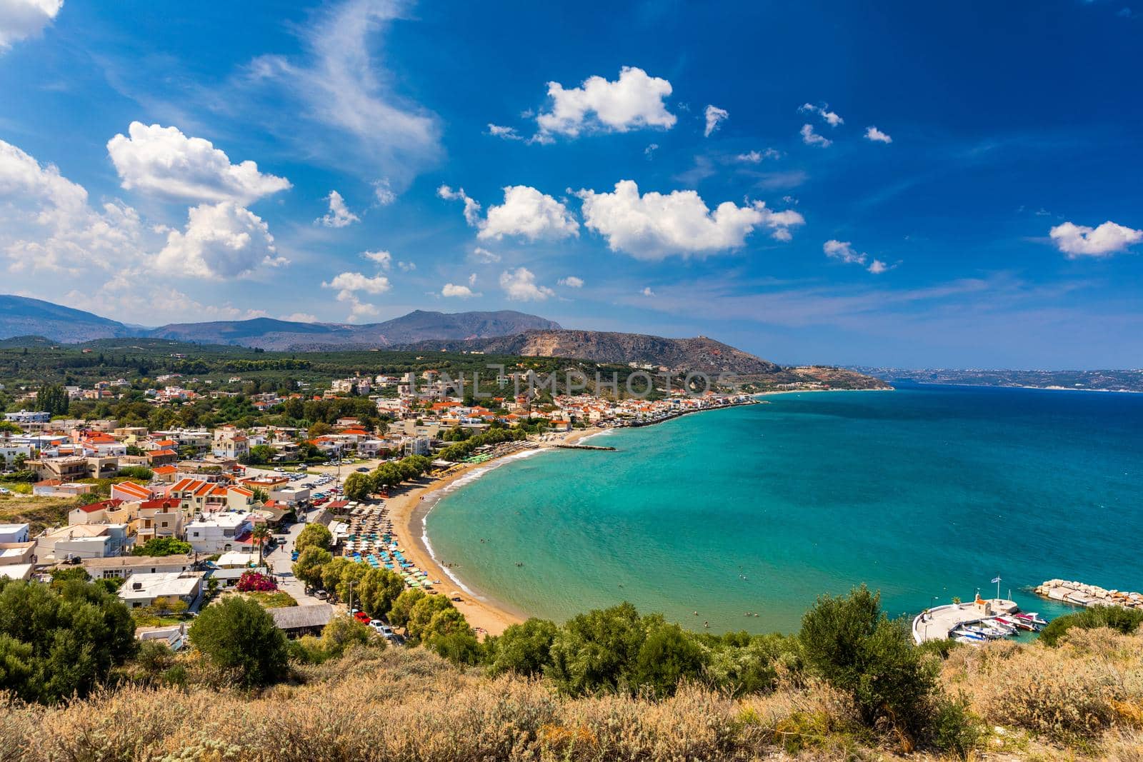 Greek holidays, beautiful Kalyves village with turquoise sea in Crete island, Greece. View of Kalyves beach, Crete. Tourists relaxing on the beach and views to the mountains, Kalyves, Crete, Greece