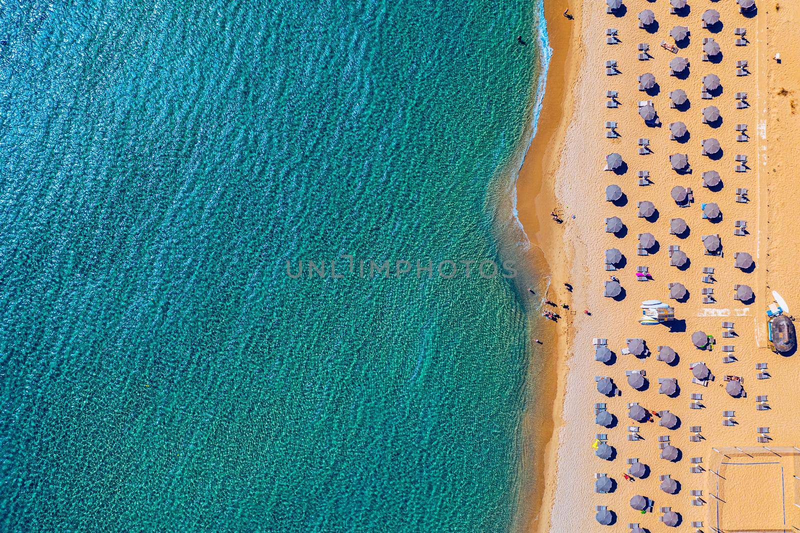 View from above, stunning aerial view of an amazing beach with beach umbrellas and turquoise clear water. Top view on sun loungers under umbrellas on the sandy beach. Concept of summer vacation. 