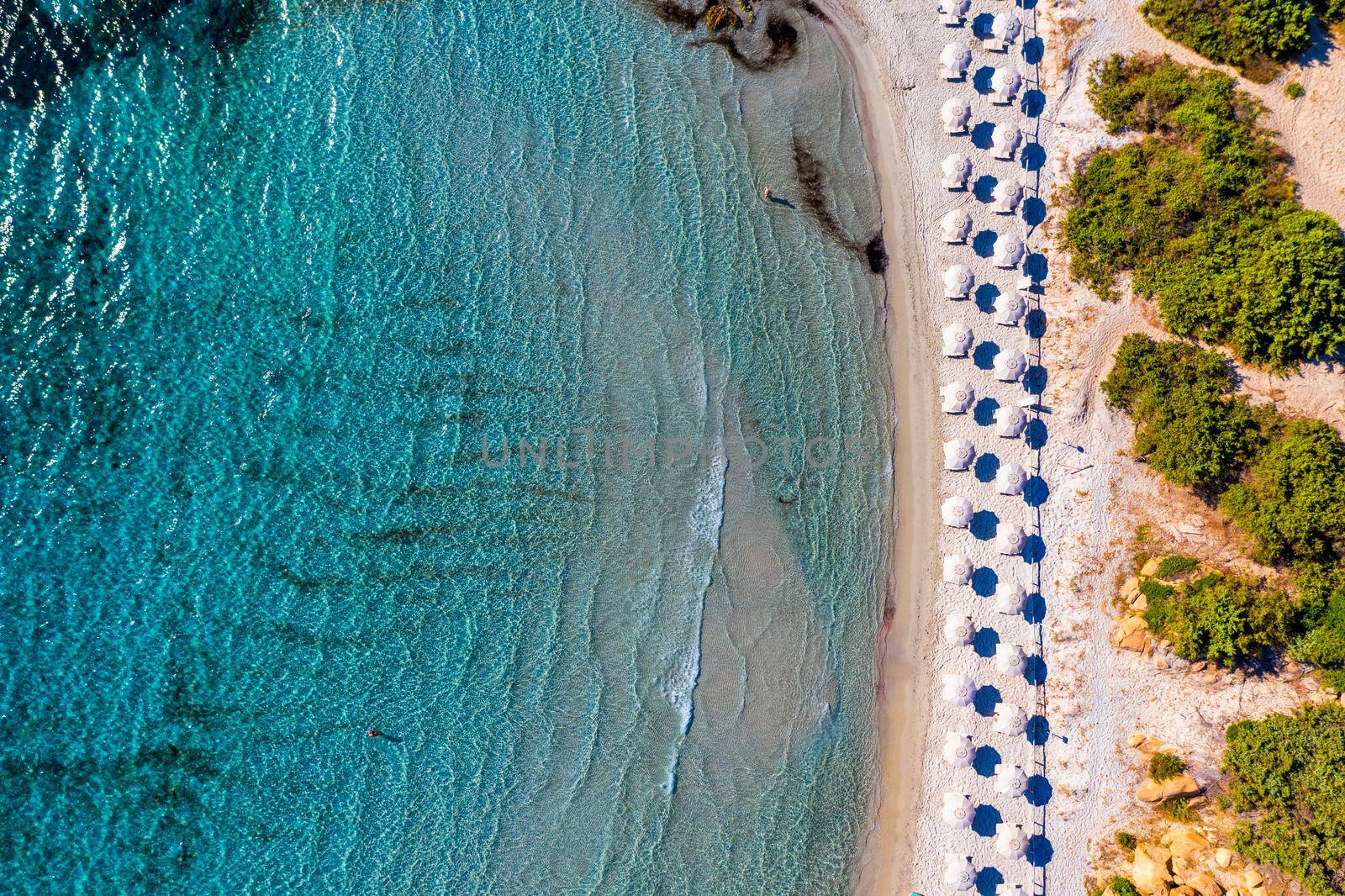 View from above, stunning aerial view of an amazing beach with beach umbrellas and turquoise clear water. Top view on sun loungers under umbrellas on the sandy beach. Concept of summer vacation. 