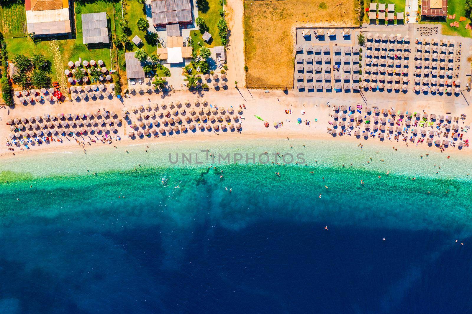 Concept of summer vacation. View from above, stunning aerial view of an amazing beach with beach umbrellas and turquoise clear water. Top view on a sun lounger under an umbrella on the sandy beach