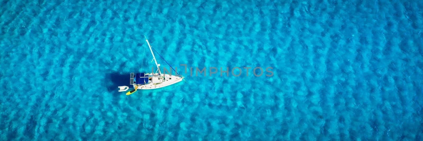 Aerial view of anchored sailing yacht in emerald sea. Aerial view of a boat. Outdoor water sports, yachting. Aerial view of anchoring yacht in open water. Ocean and sea travel and transportation by DaLiu