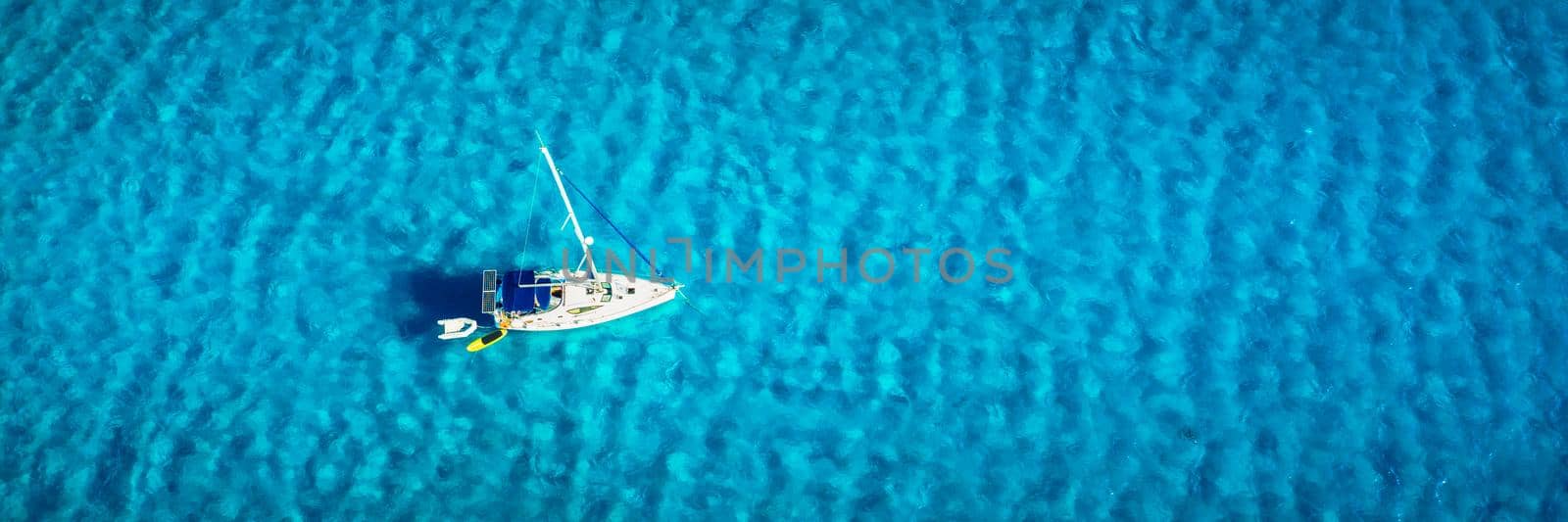 Aerial view of anchored sailing yacht in emerald sea. Aerial view of a boat. Outdoor water sports, yachting. Aerial view of anchoring yacht in open water. Ocean and sea travel and transportation