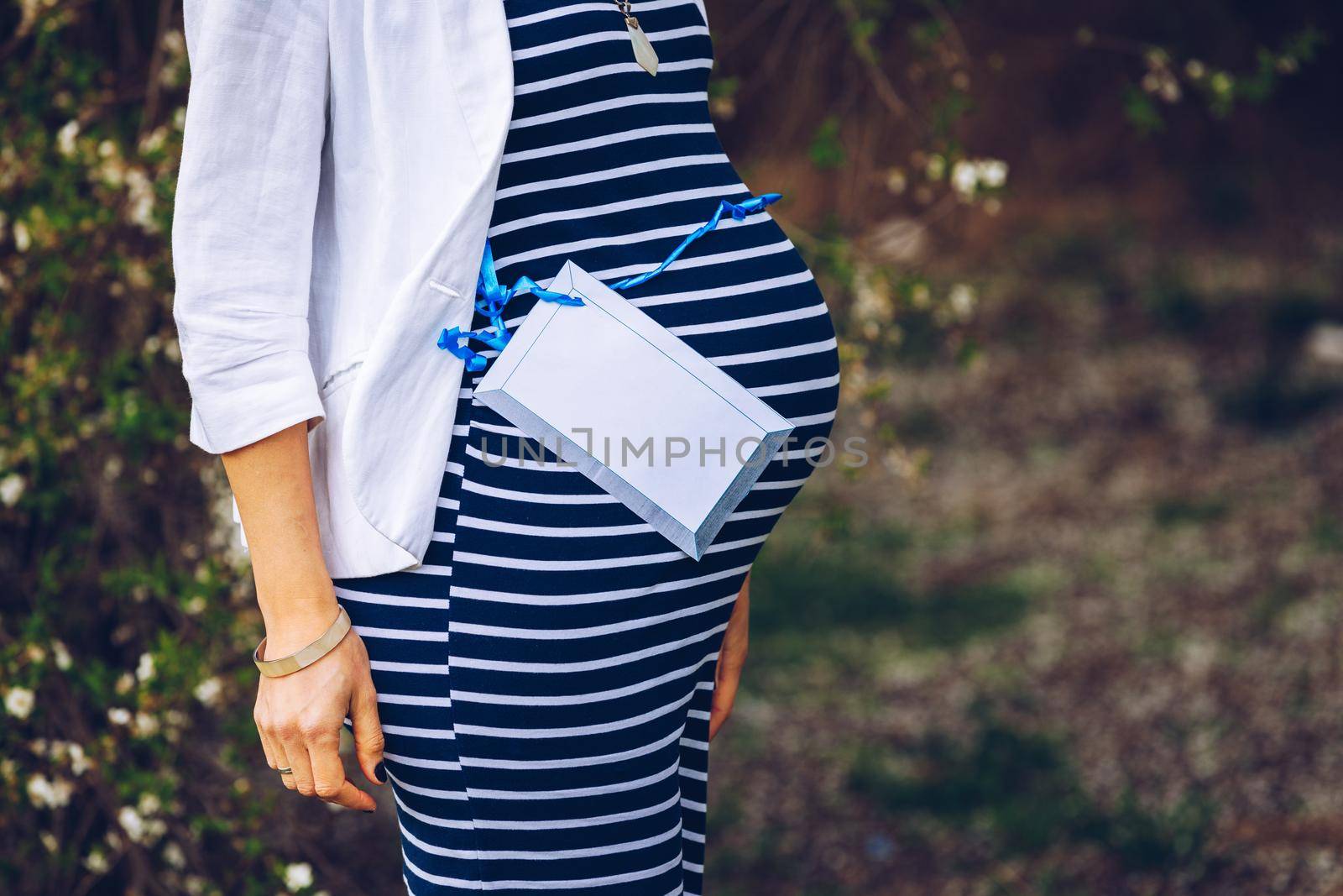 Beautiful pregnant woman feeling happy in nature while taking care of her child. Young expecting mother holding baby in pregnant belly. Maternity prenatal care and woman pregnancy concept.
