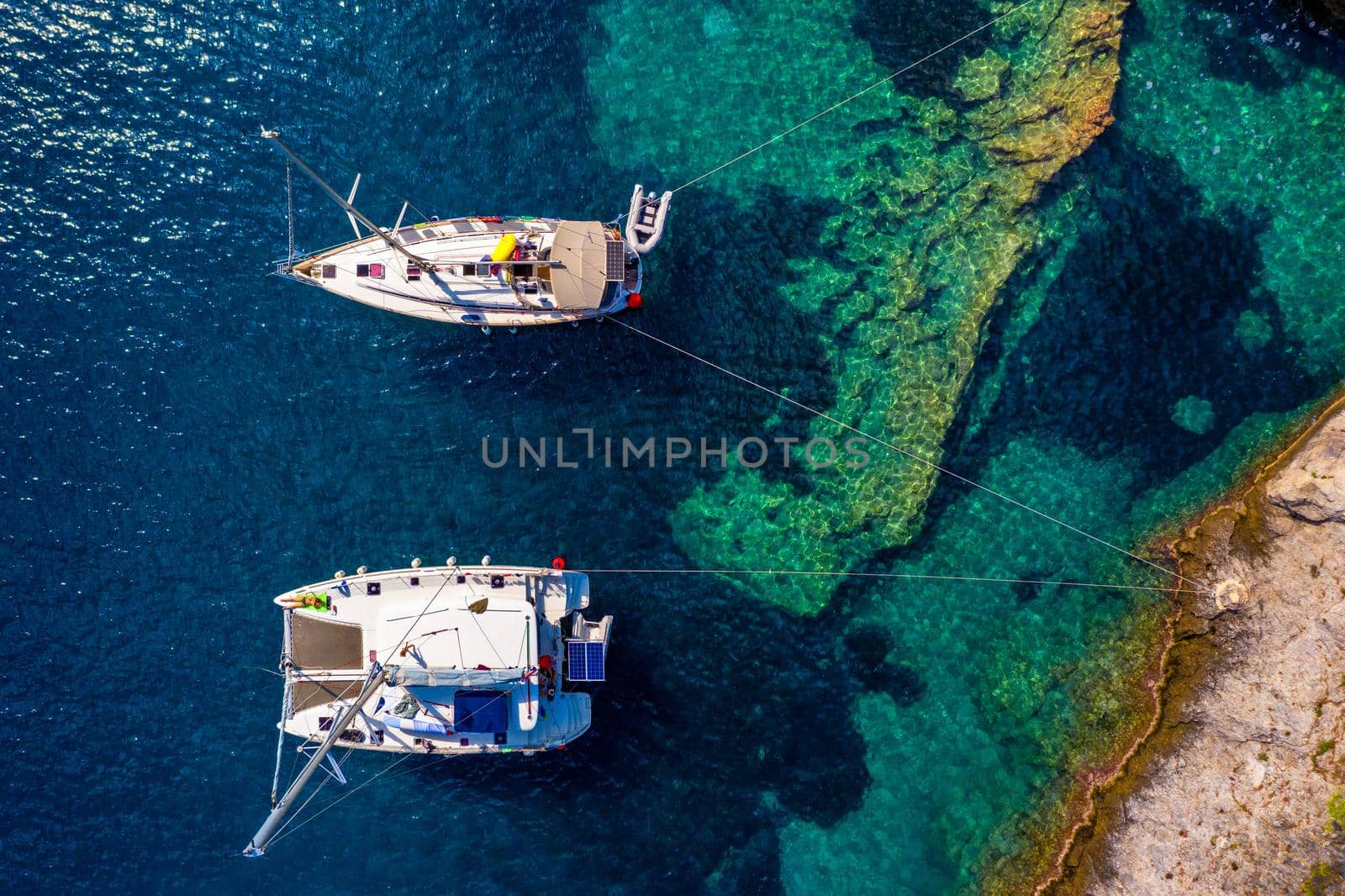 Aerial view of anchored sailing yacht in emerald sea. Aerial view of a boat. Outdoor water sports, yachting. Aerial view of anchoring yacht in open water. Ocean and sea travel and transportation