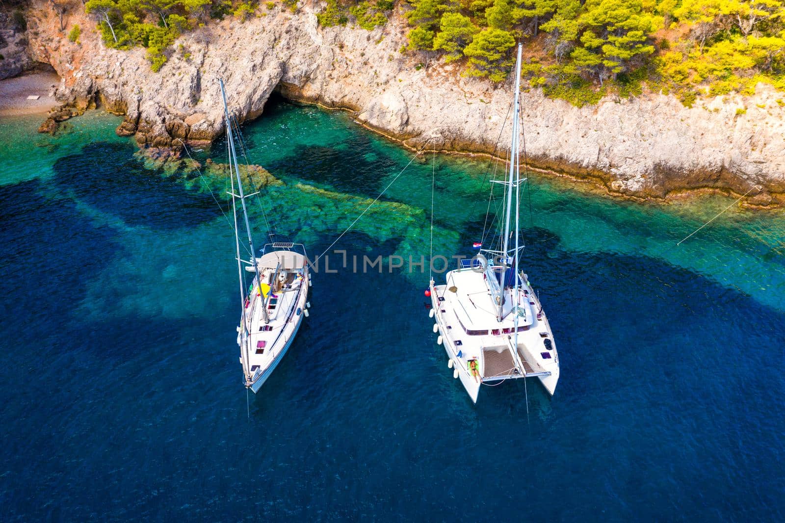 Yacht anchoring in crystal clear turquoise water in front of the tropical island, alternative lifestyle, living on a boat. Aerial view of yacht at anchor on turquoise water, showing luxury, wealth.