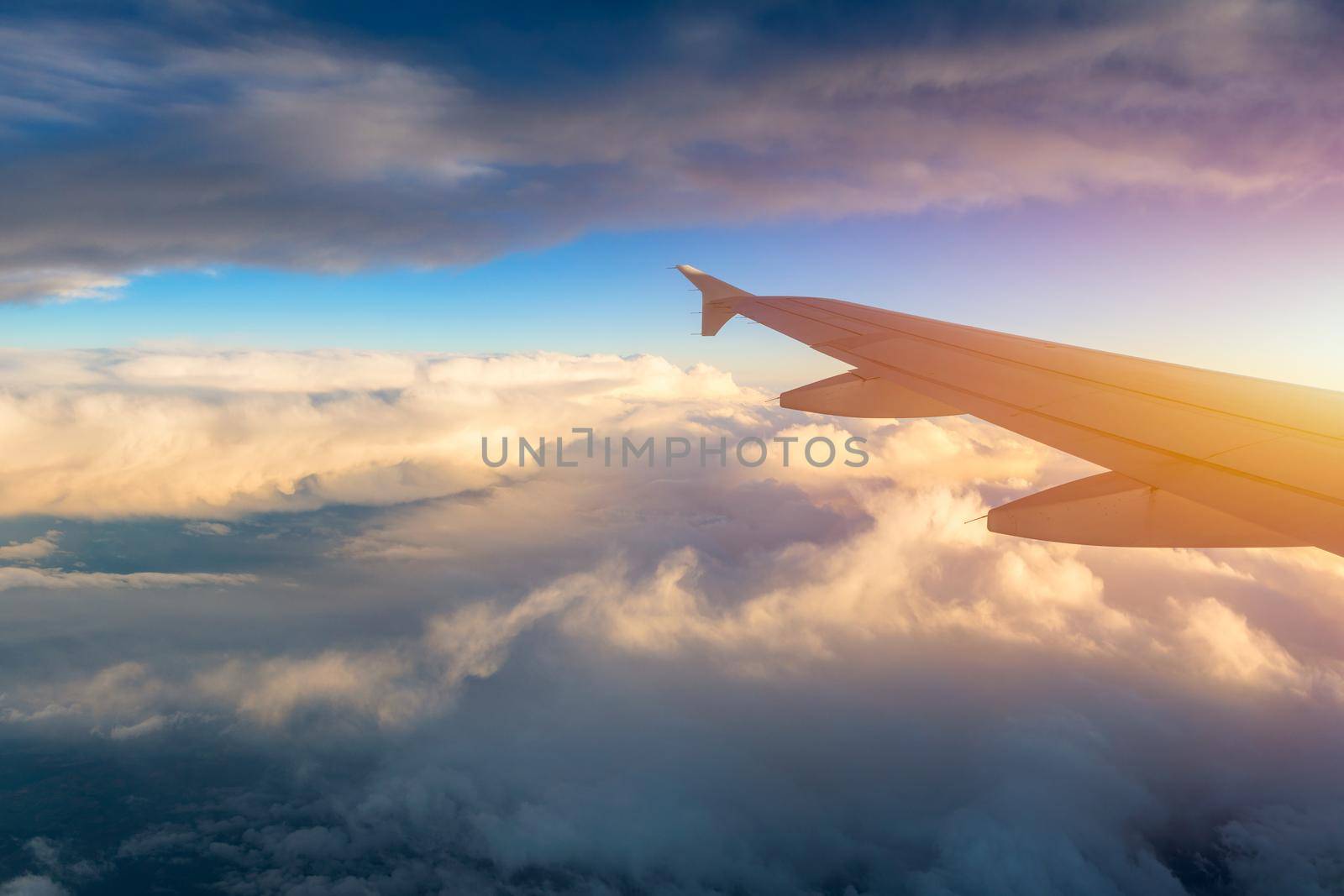 Flying and traveling, view from airplane window on the wing on sunset time. Aircraft wing under the earth and clouds. Flight in sky. Looking over aircraft wing in flight. 
