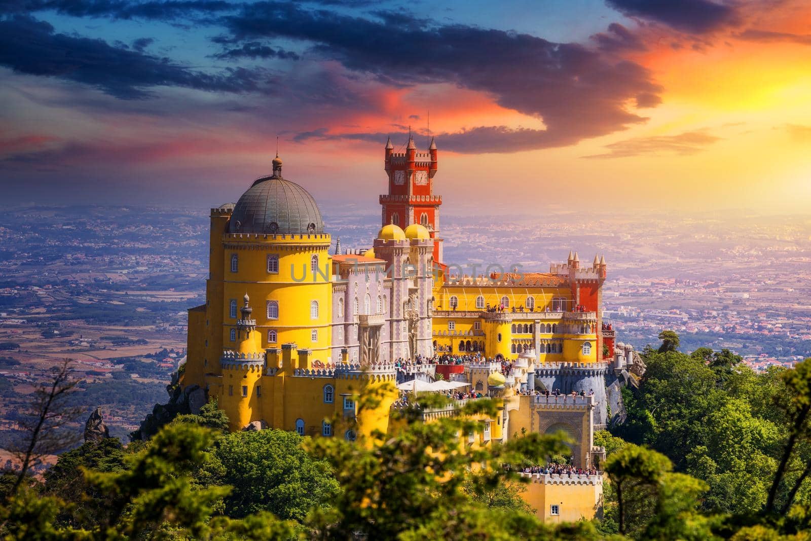 Famous historic Pena palace part of cultural site of Sintra against sunset sky in Portugal. Panoramic View Of Pena Palace, Sintra, Portugal. Pena National Palace at sunset, Sintra, Portugal. 