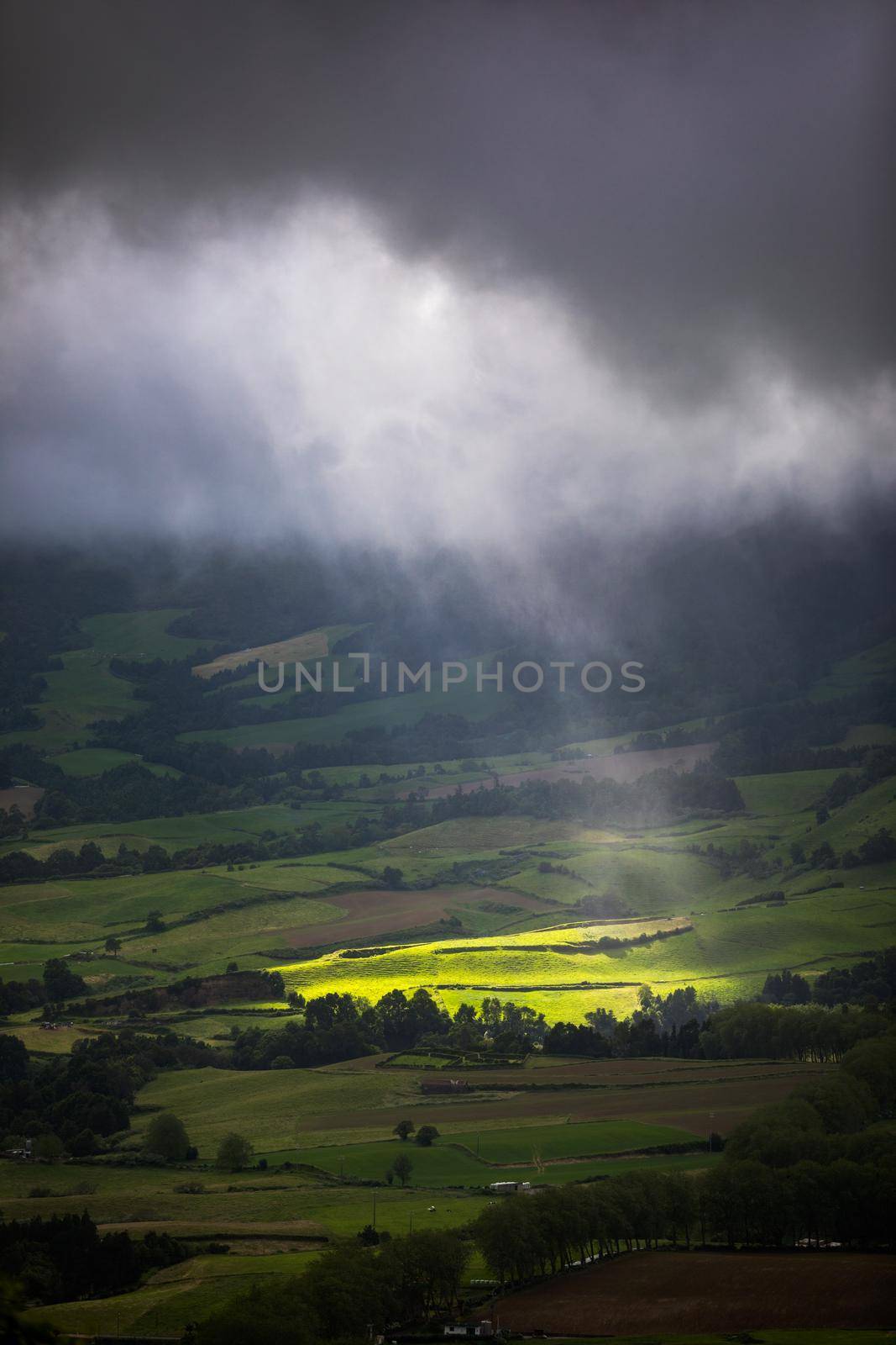 Bright sunlight shining through hole of clouds to dark scene of mountain range, Azores, Sao Miguel, Portugal. The beam of light through the dark clouds on the mountains in Azores, Portugal.