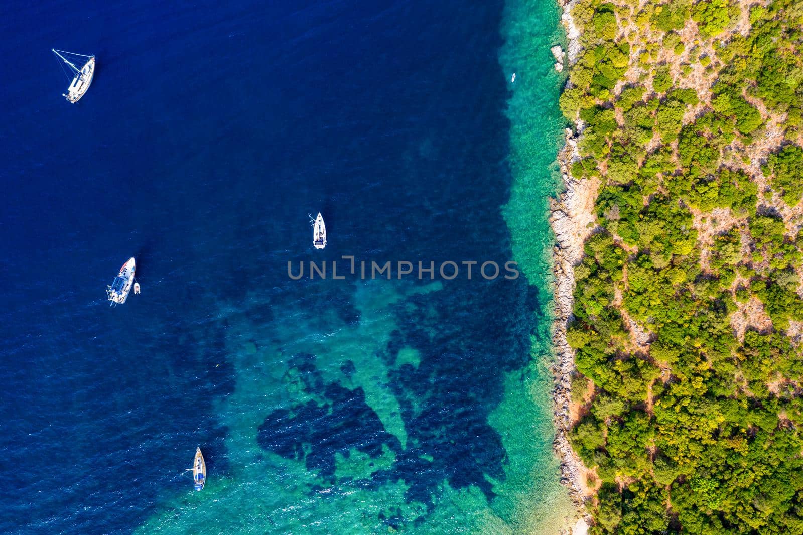Yacht anchoring in crystal clear turquoise water in front of the tropical island, alternative lifestyle, living on a boat. Aerial view of yacht at anchor on turquoise water, showing luxury, wealth.