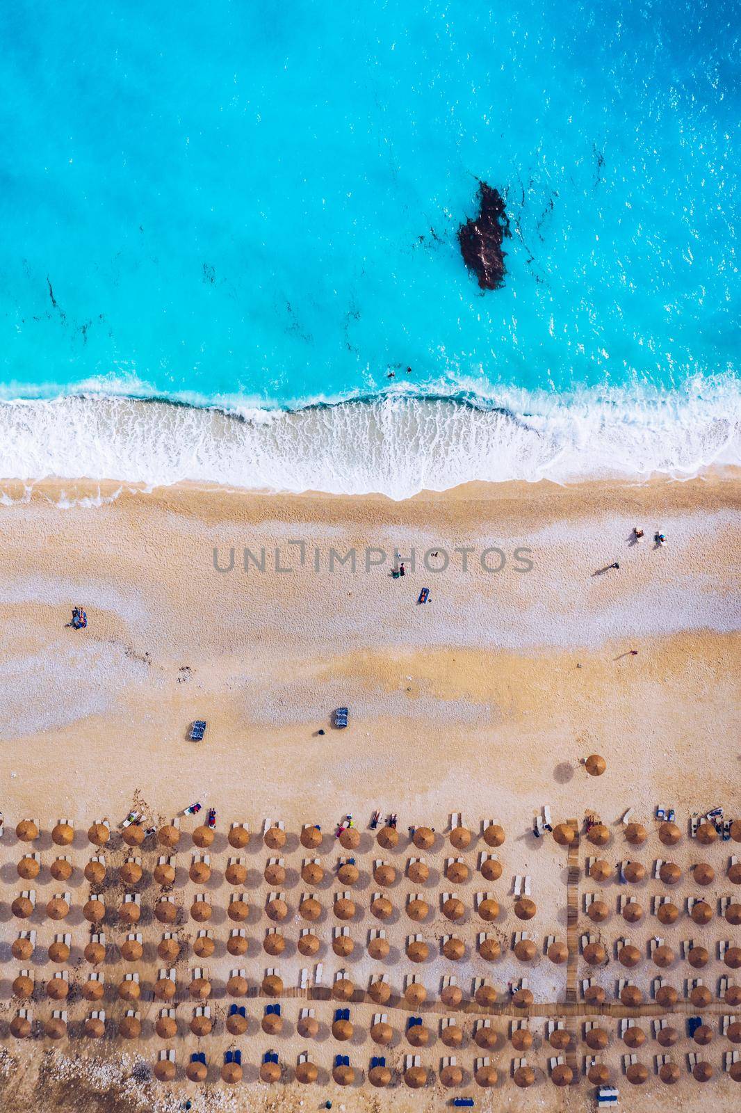 View from above, stunning aerial view of an amazing beach with beach umbrellas and turquoise clear water. Top view on sun loungers under umbrellas on the sandy beach. Concept of summer vacation. 