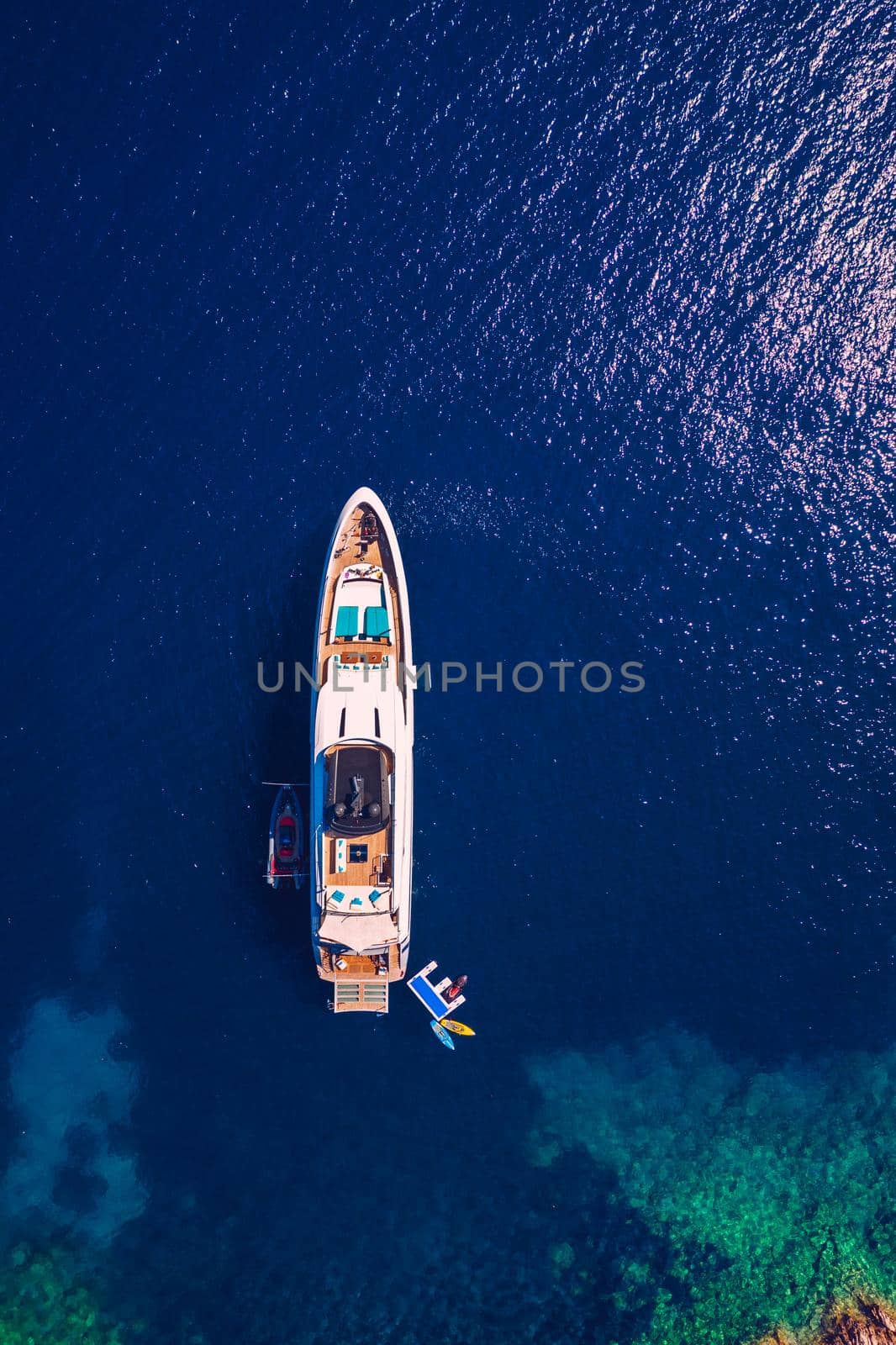 Yacht anchoring in crystal clear turquoise water in front of the tropical island, alternative lifestyle, living on a boat. Aerial view of yacht at anchor on turquoise water, showing luxury, wealth.