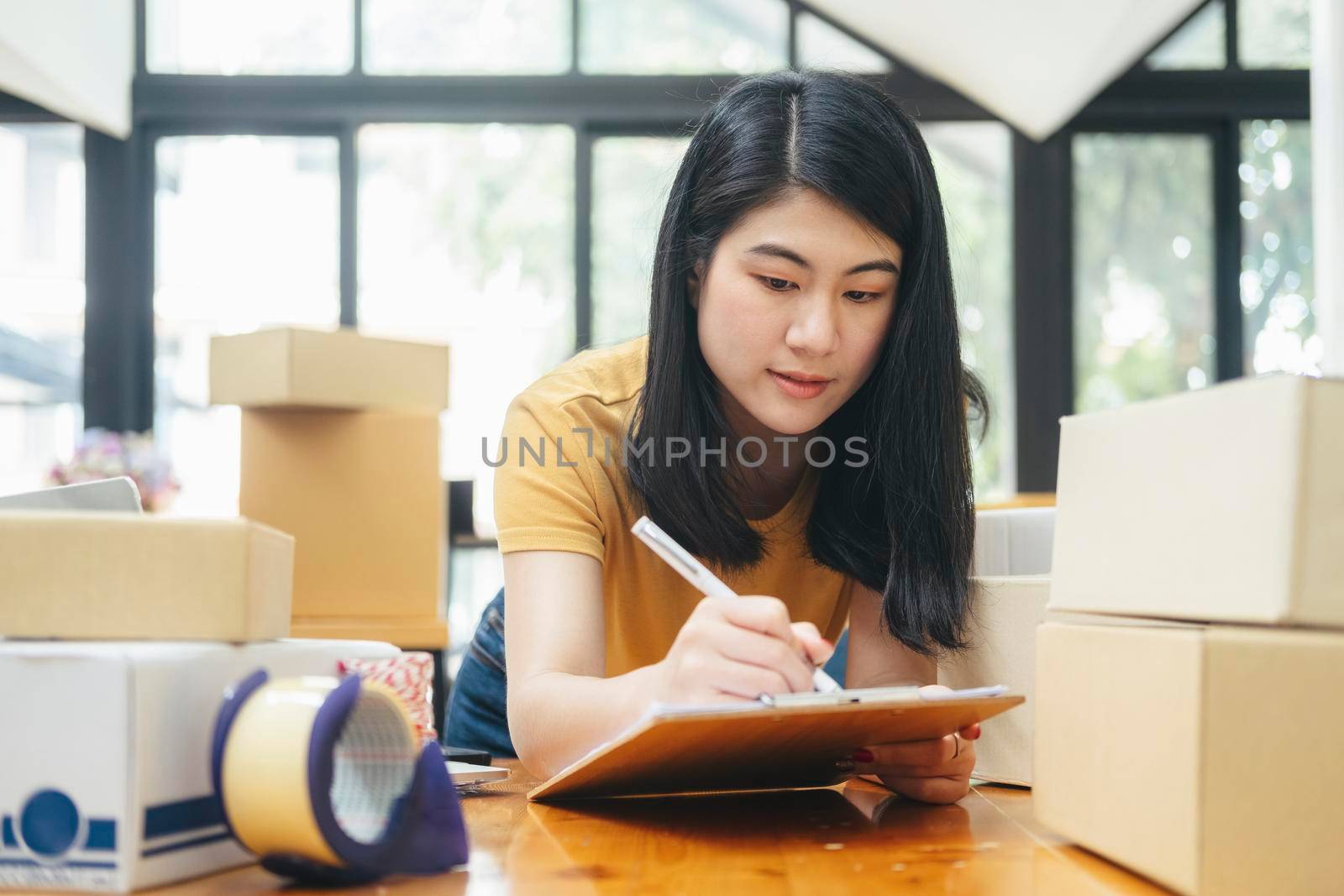 Young business startup online seller owner using computer for checking the customer orders from email or website and preparing packages for product office equipment.