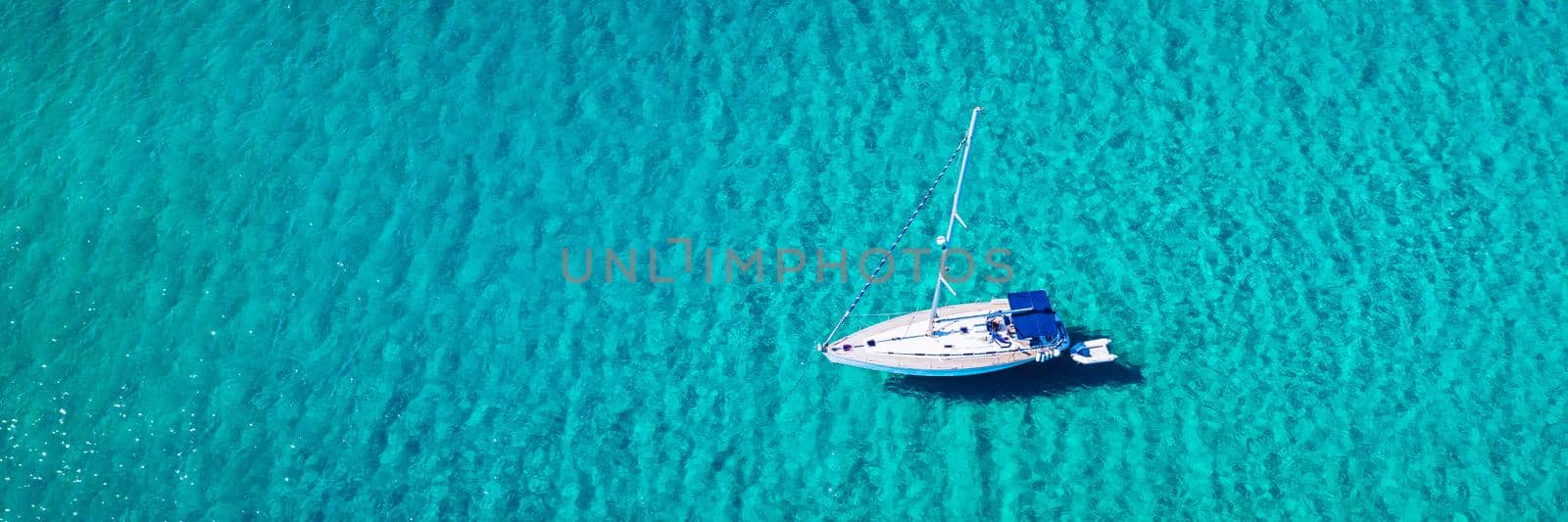 Aerial view of anchored sailing yacht in emerald sea. Aerial view of a boat. Outdoor water sports, yachting. Aerial view of anchoring yacht in open water. Ocean and sea travel and transportation