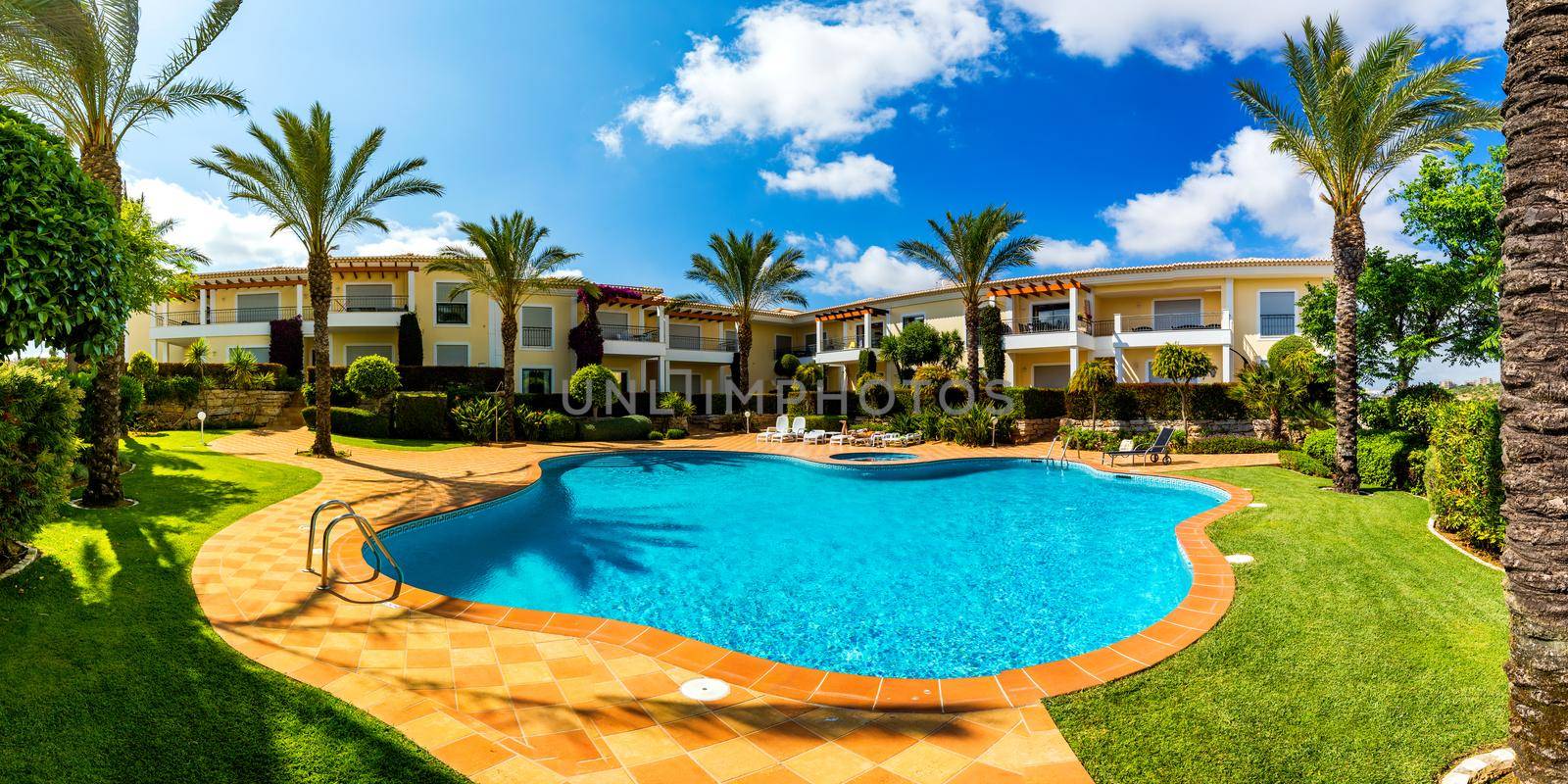 Swimming pool, sun-loungers and palm trees during a warm sunny day, paradise destination for vacations. Backyard swimming pool with garden full of palm trees and flowers. Backyard with swimming pool.