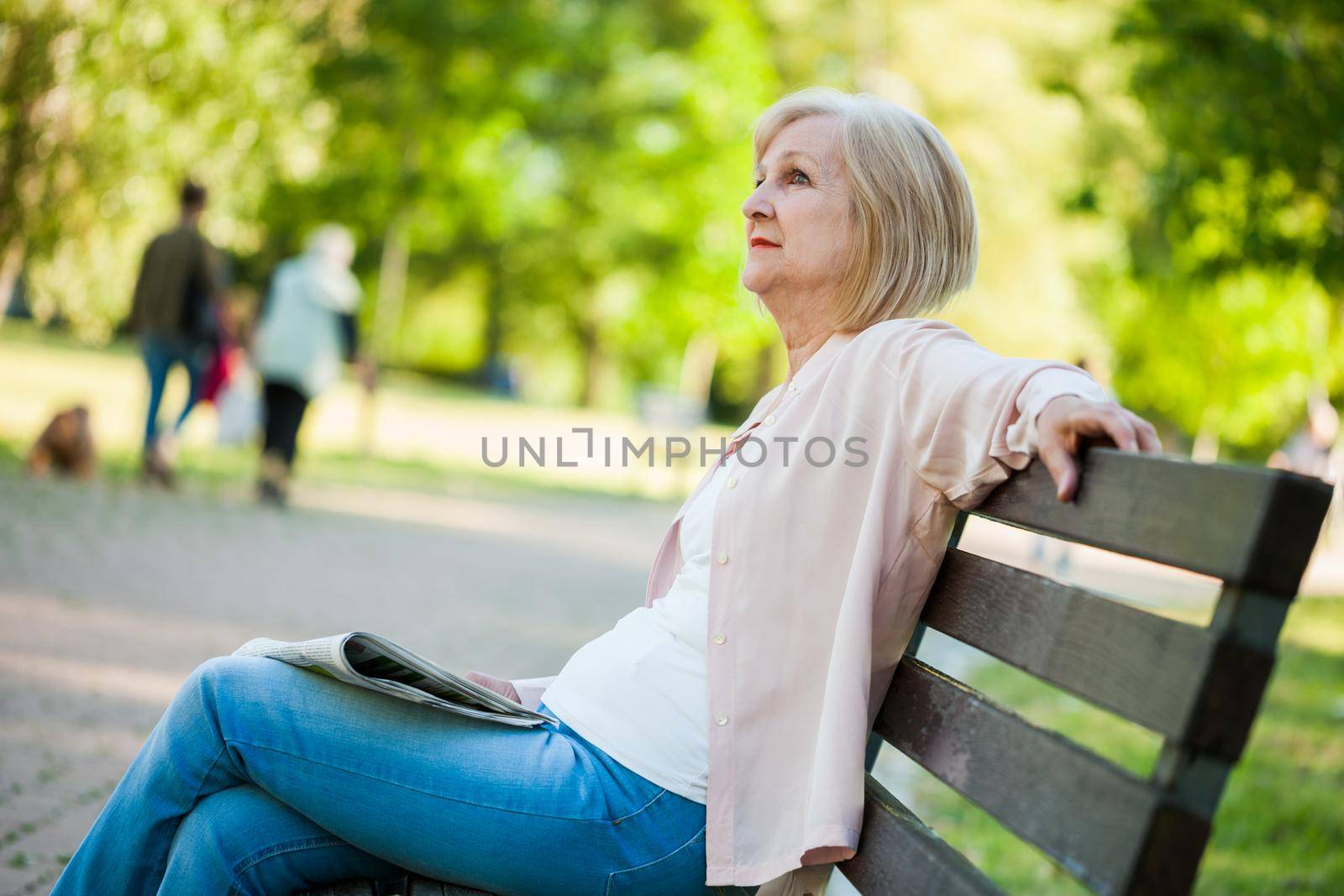 Adult woman sitting in park and reading newspapers.