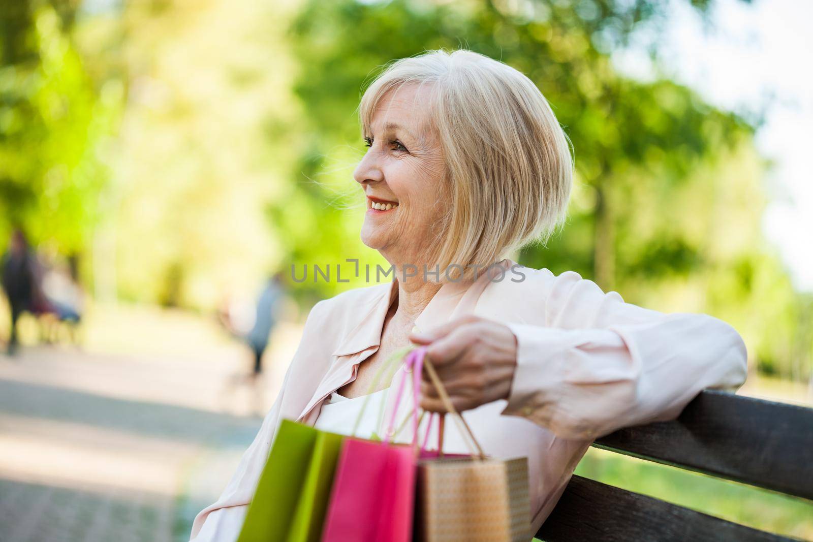 Happy adult woman sitting in park after shopping.