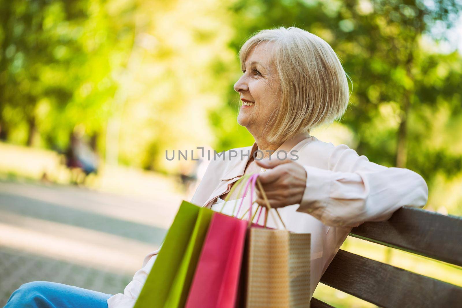 Happy adult woman sitting in park after shopping.