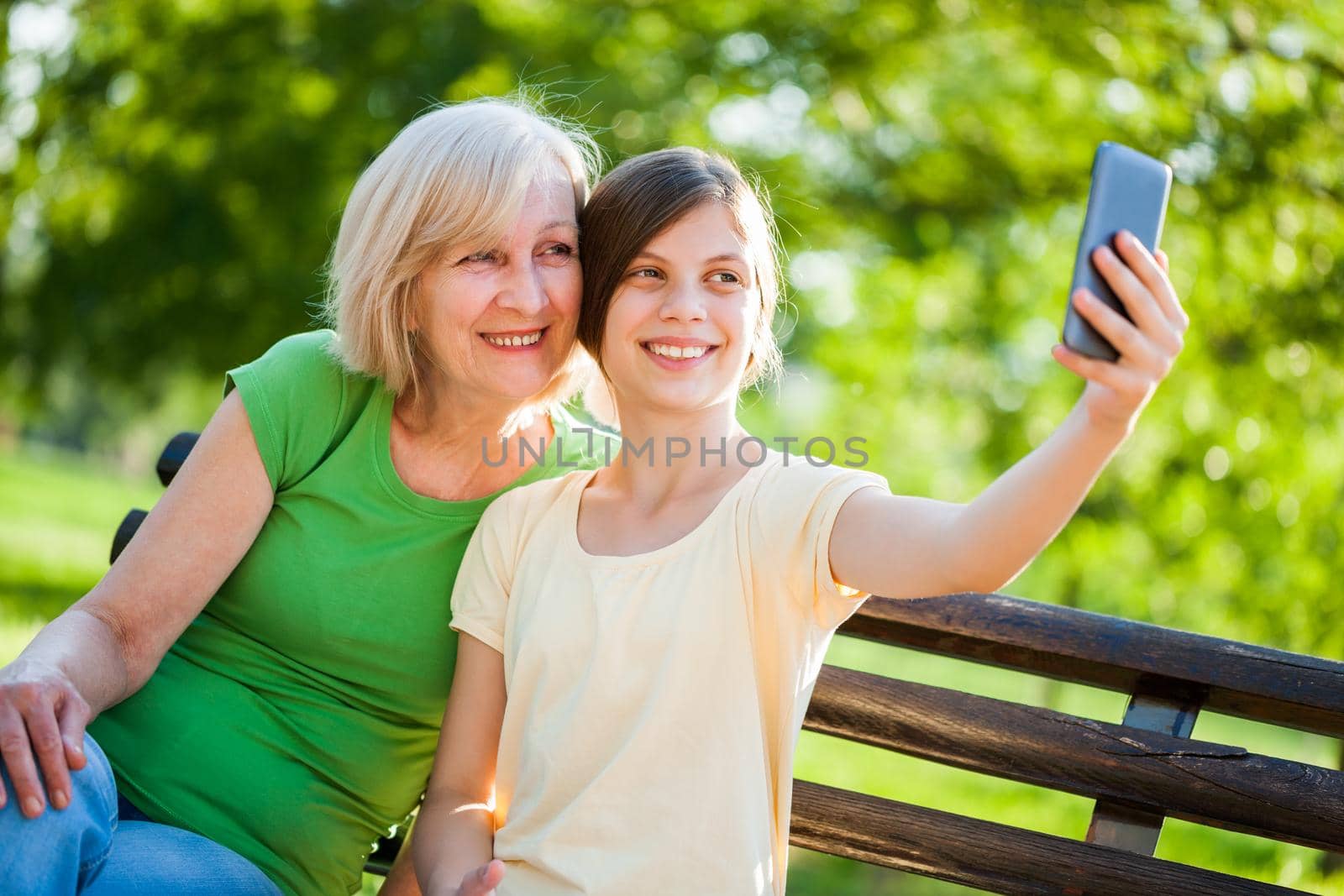Grandmother and granddaughter are sitting in park and taking selfie.