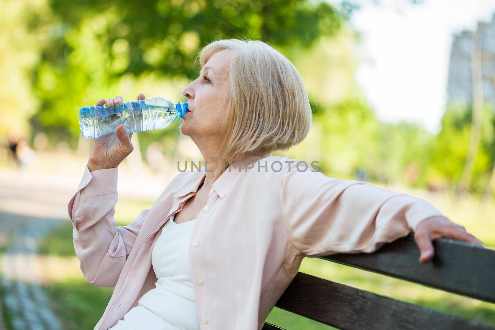 Adult woman is sitting in park and drinking water.