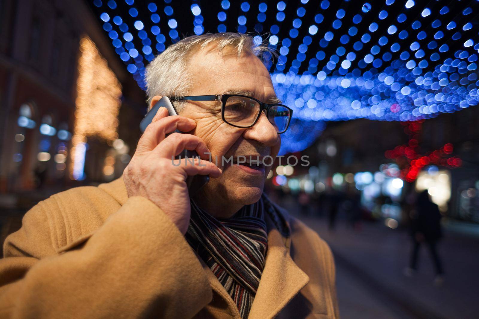 Outdoor portrait of happy senior man in city. He is talking on phone.