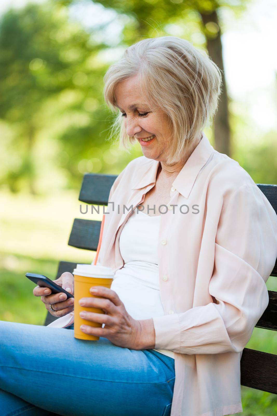 Happy adult woman sitting in park and using smartphone.