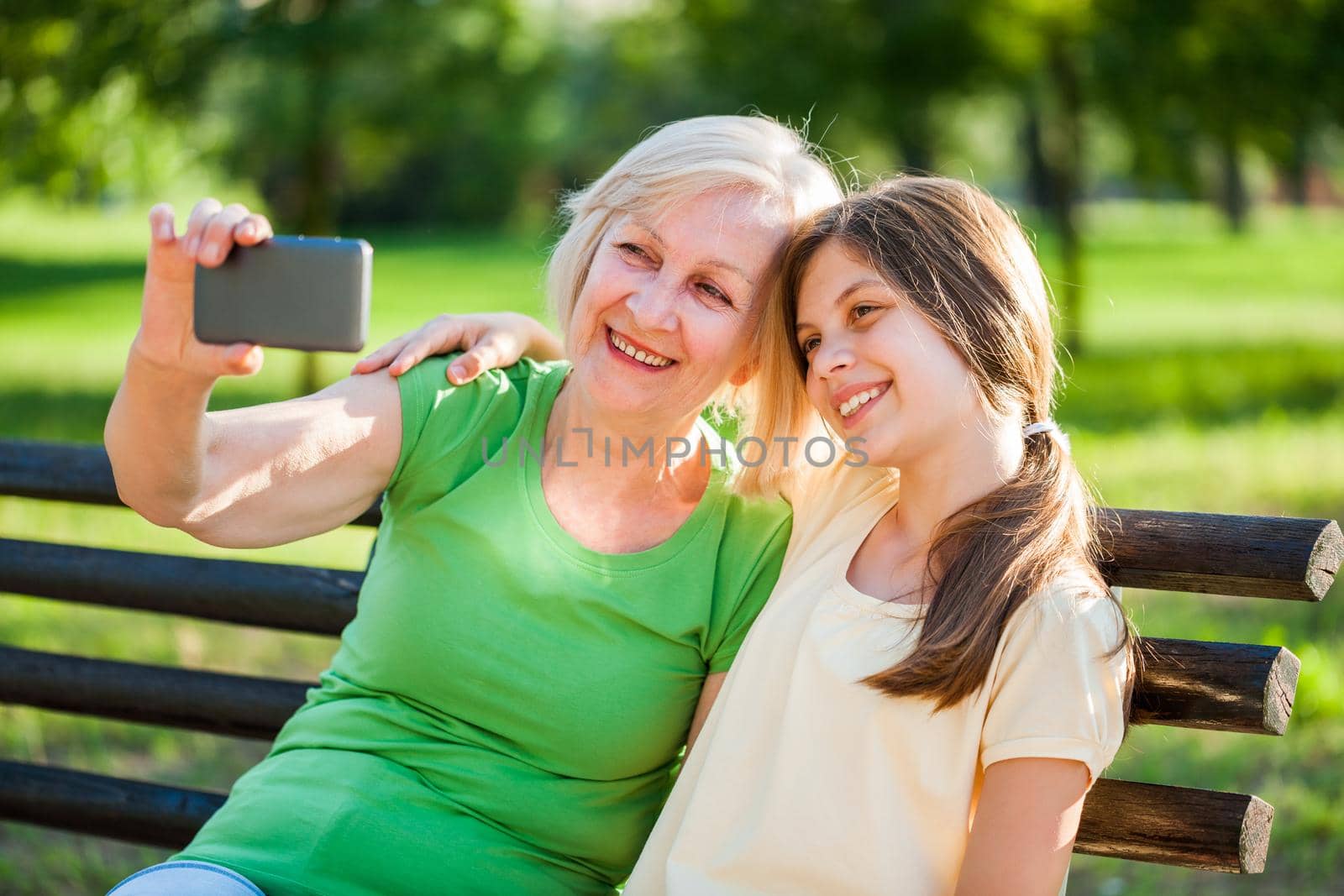 Grandmother and granddaughter are sitting in park and taking selfie.
