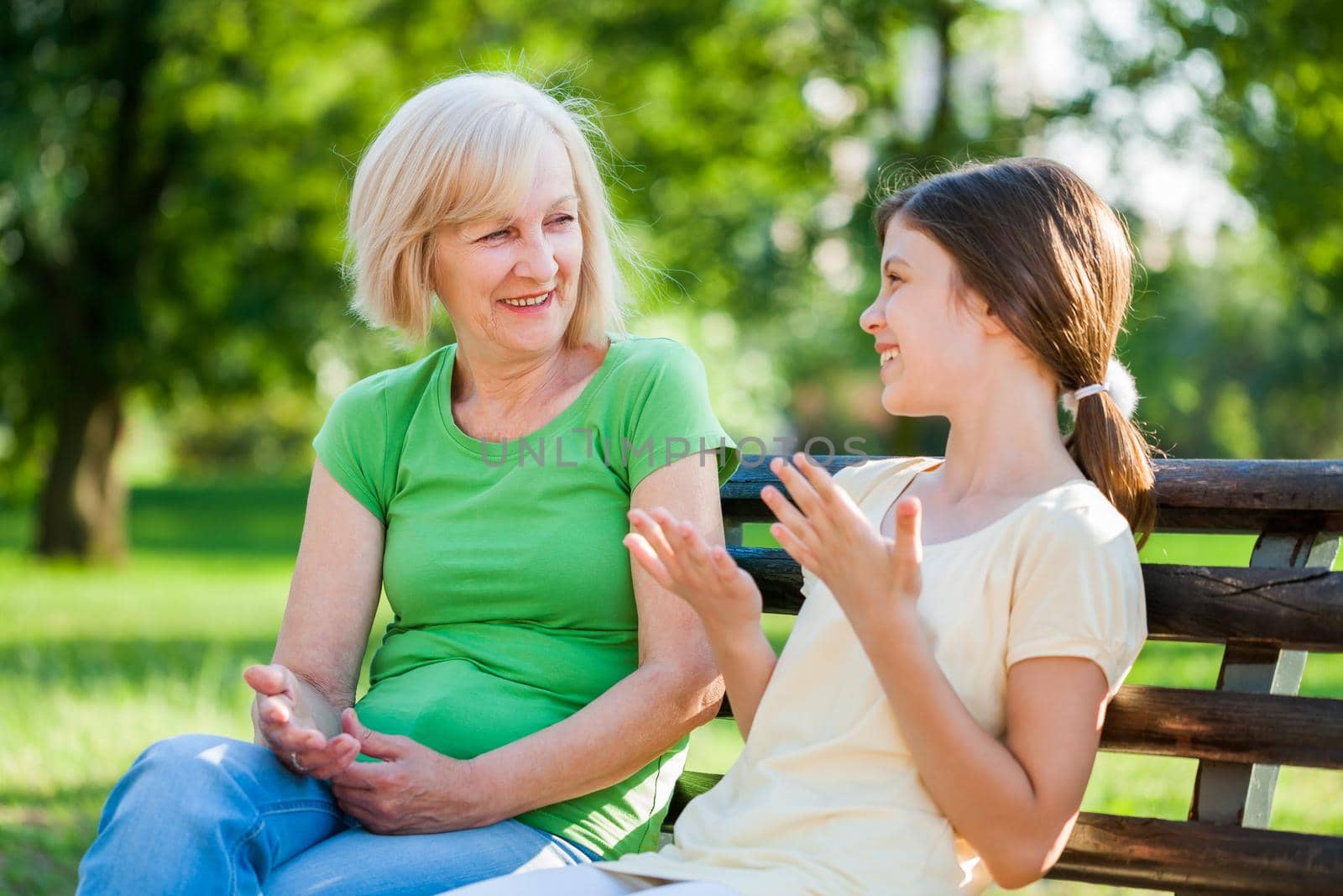 Grandmother and granddaughter are sitting in park and talking.