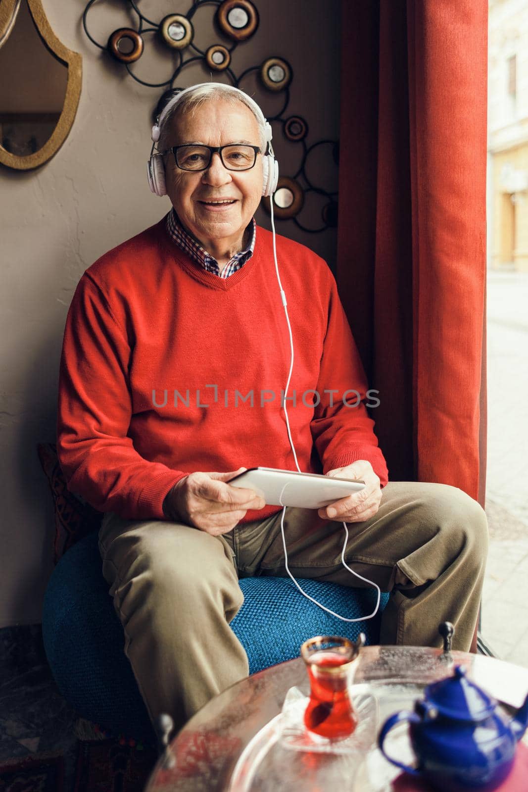 Portrait of happy senior man who is chatting on digital tablet in a cafe.