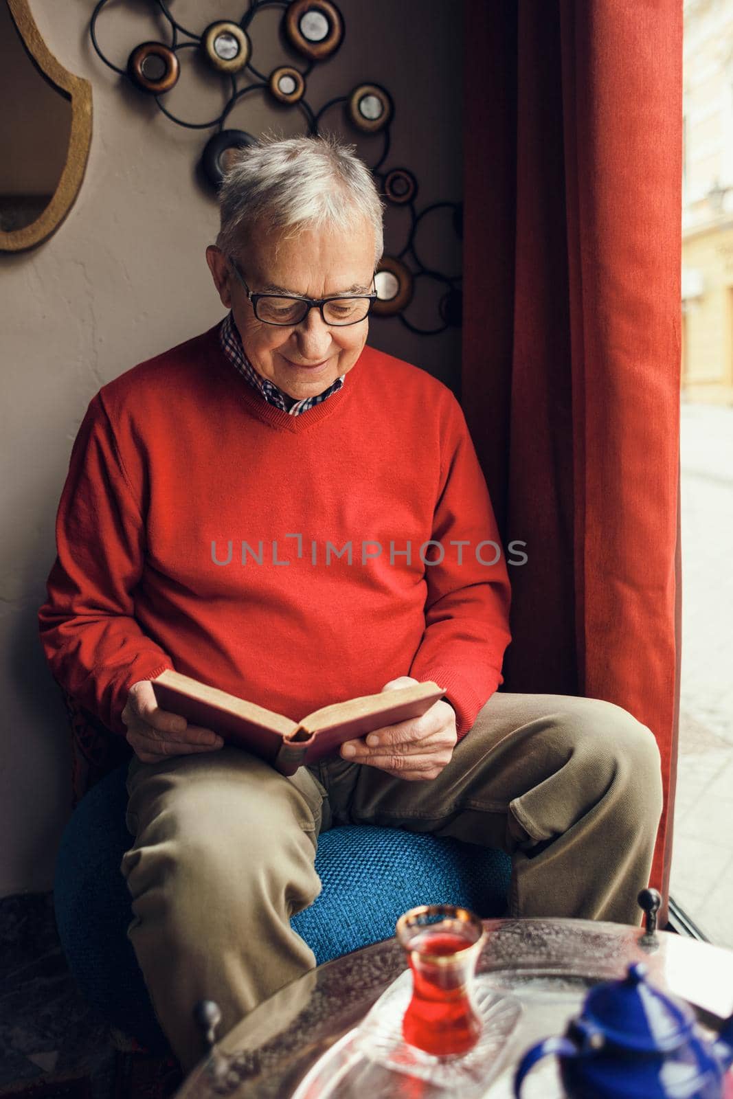 Senior man is sitting in cafe and reading a book.