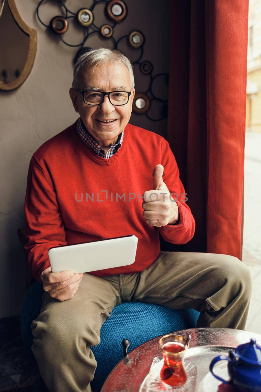 Portrait of happy senior man who is using digital tablet in a cafe.