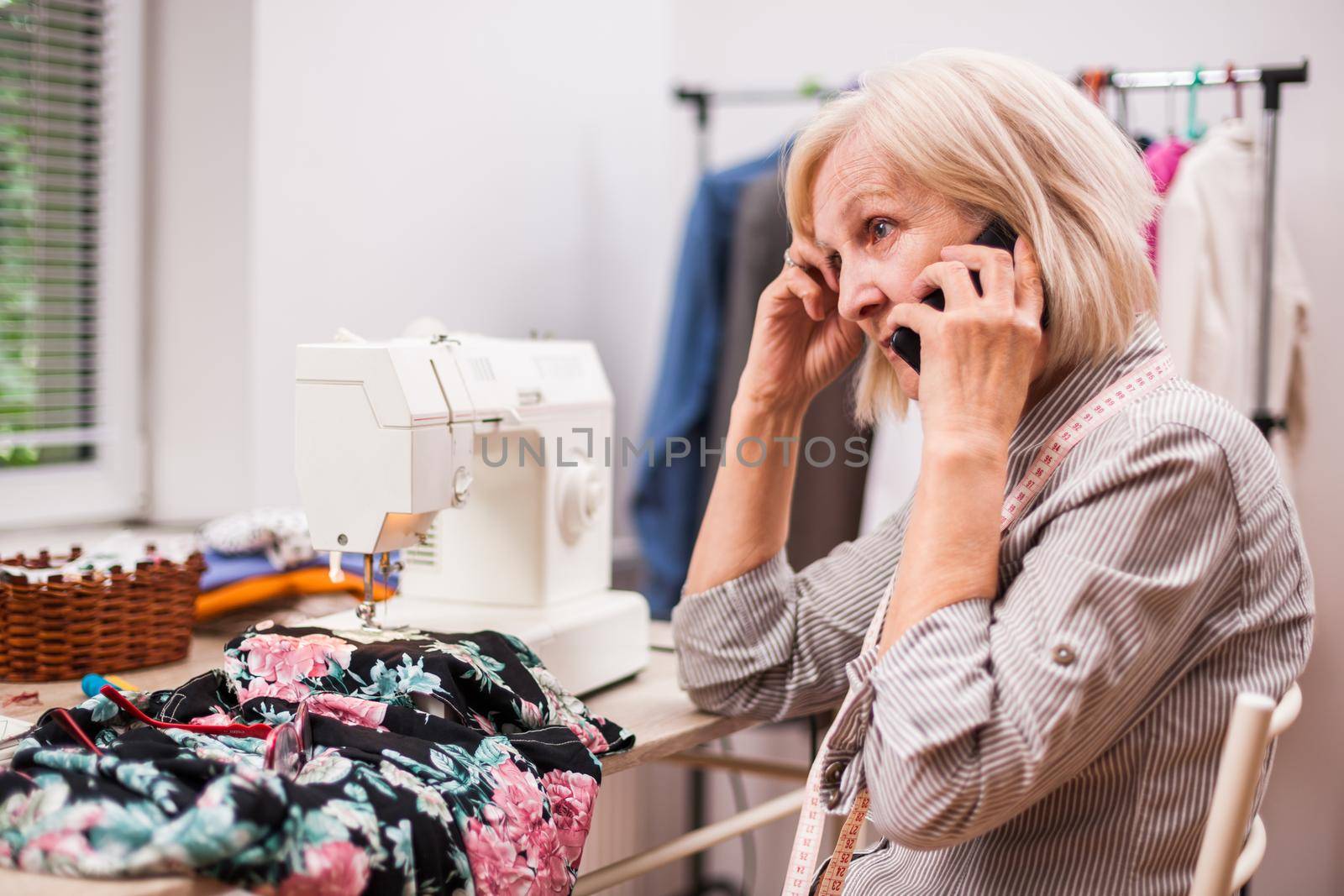 Adult woman is sewing in her studio. She is talking with client.