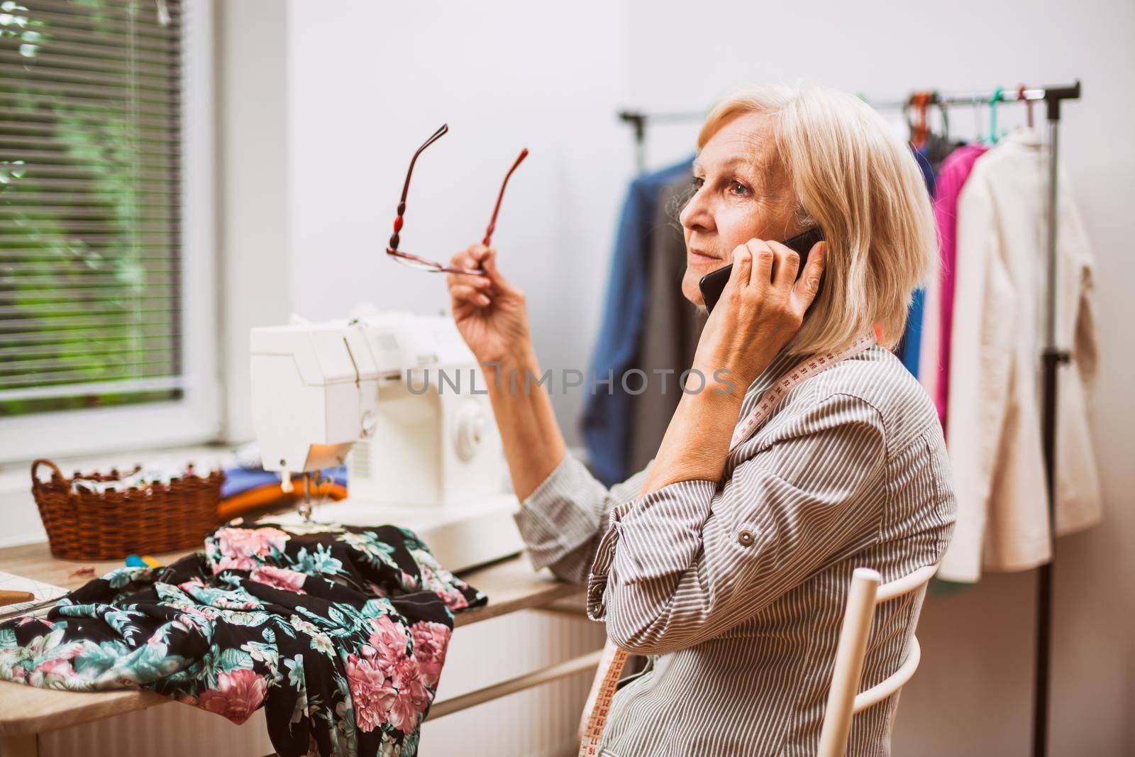 Adult woman is sewing in her studio. She is talking with client.