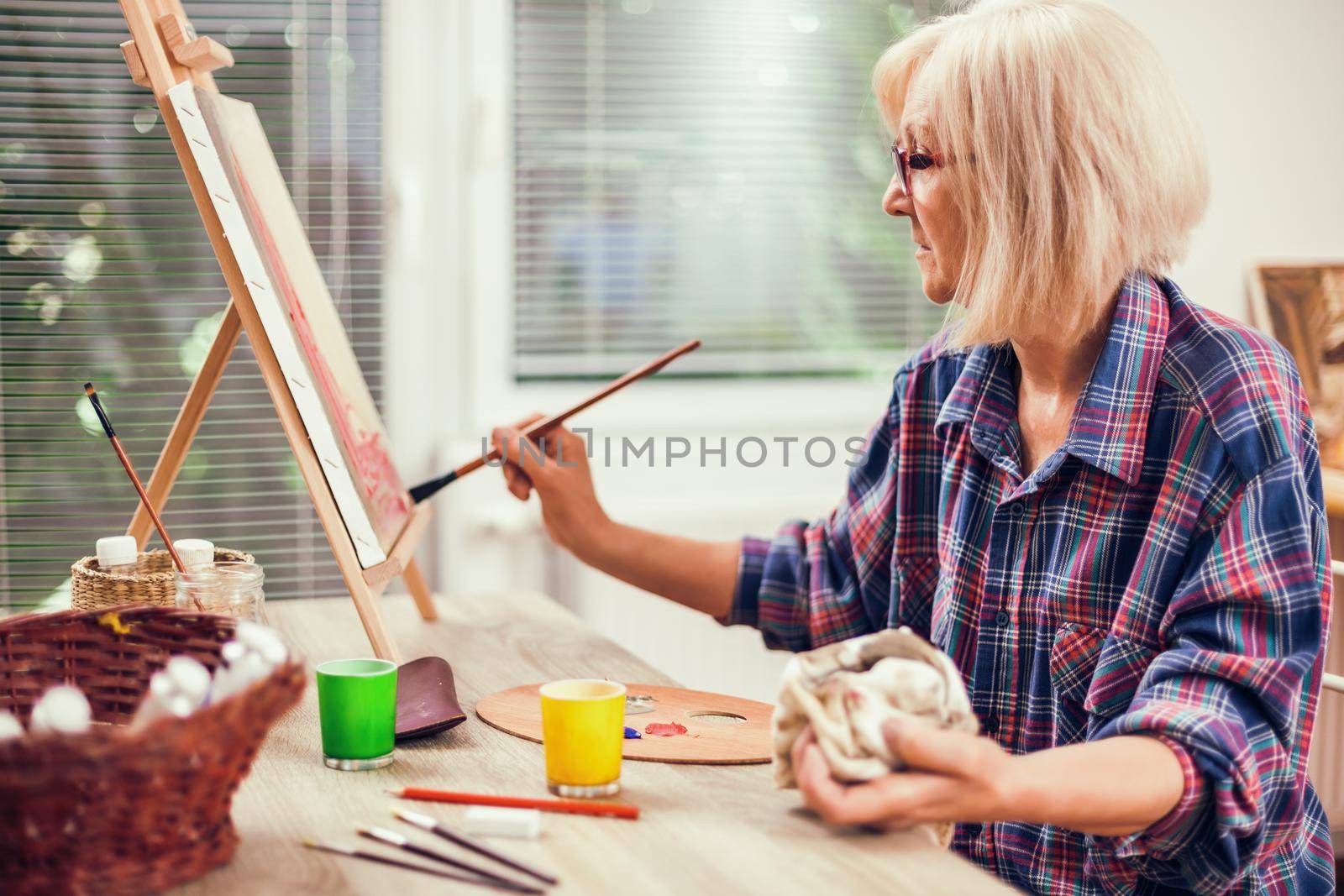 Elderly woman is painting in her home. Retirement hobby.