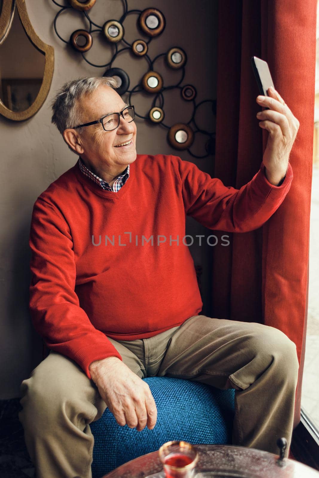 Portrait of senior man who is taking selfie in a cafe.