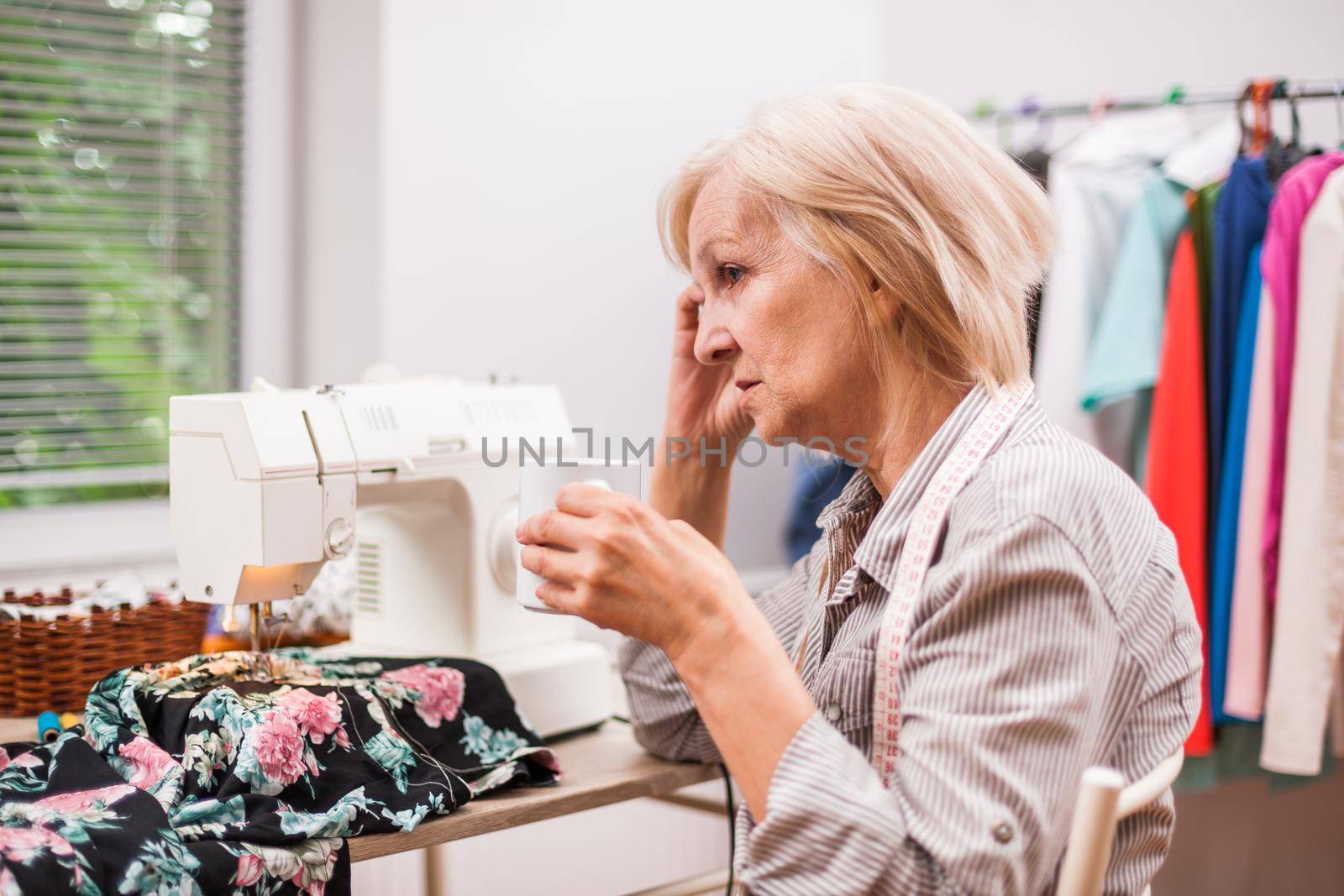 Adult woman is sewing in her studio. She is tired.