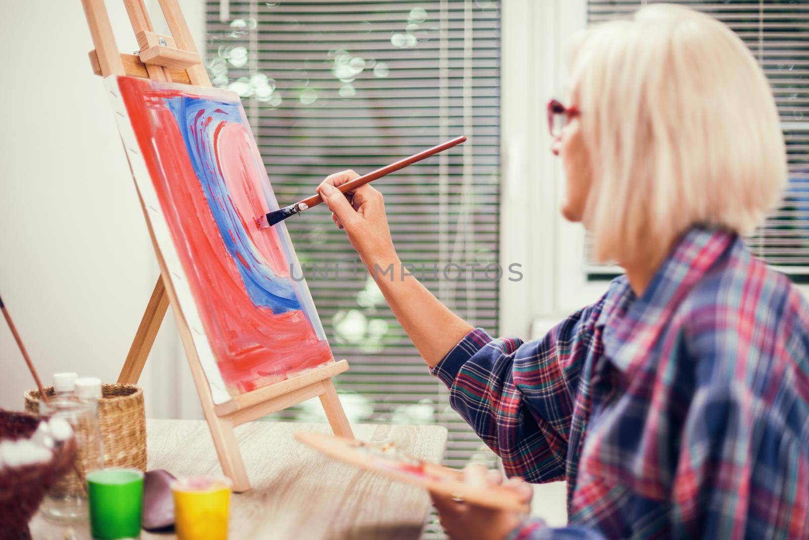 Elderly woman is painting in her home. Retirement hobby.