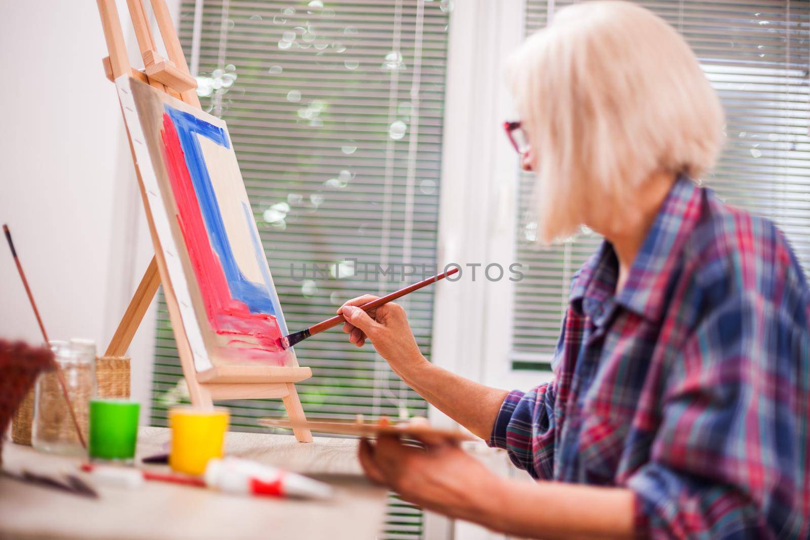 Elderly woman is painting in her home. Retirement hobby.