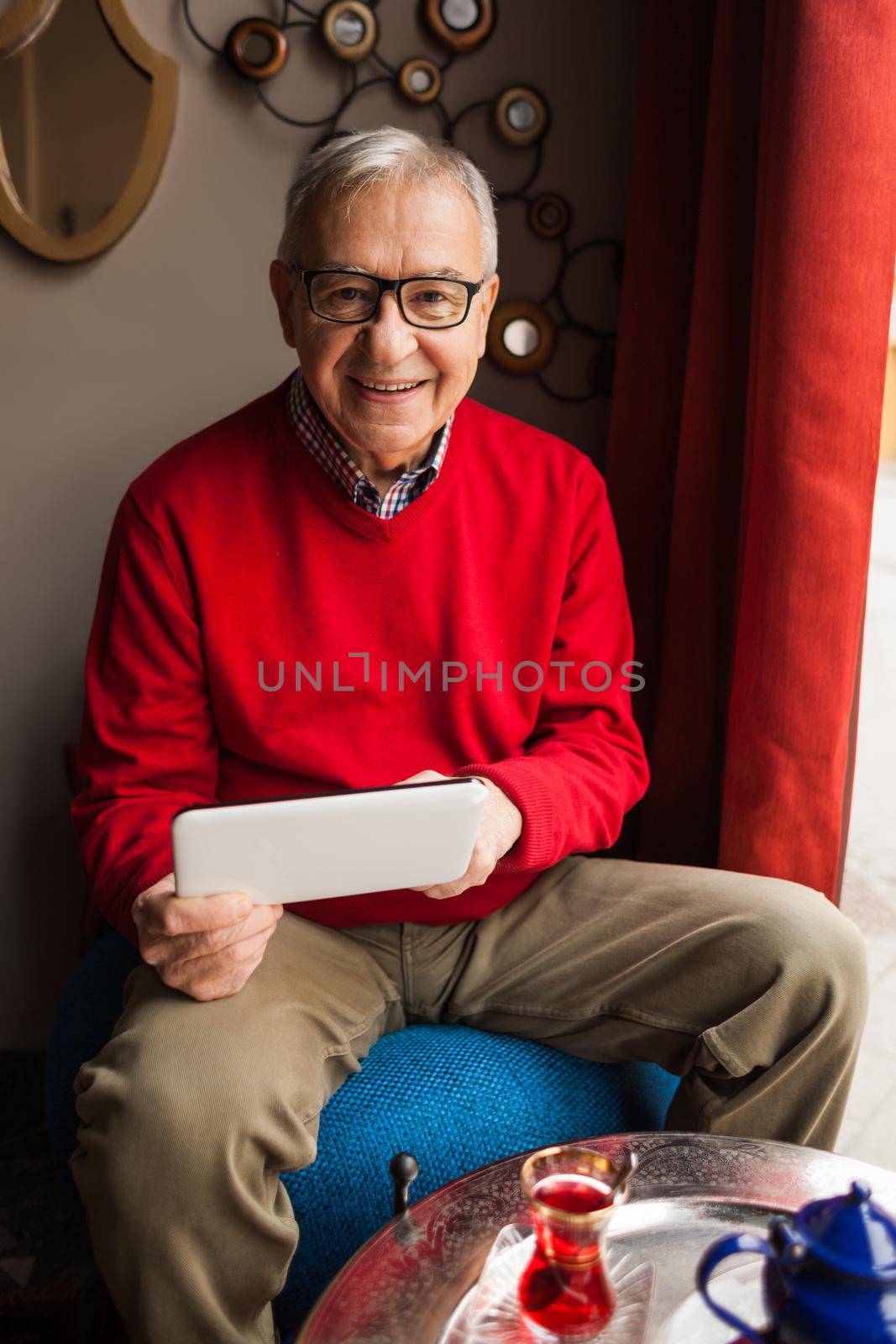 Portrait of happy senior man who is using digital tablet in a cafe.