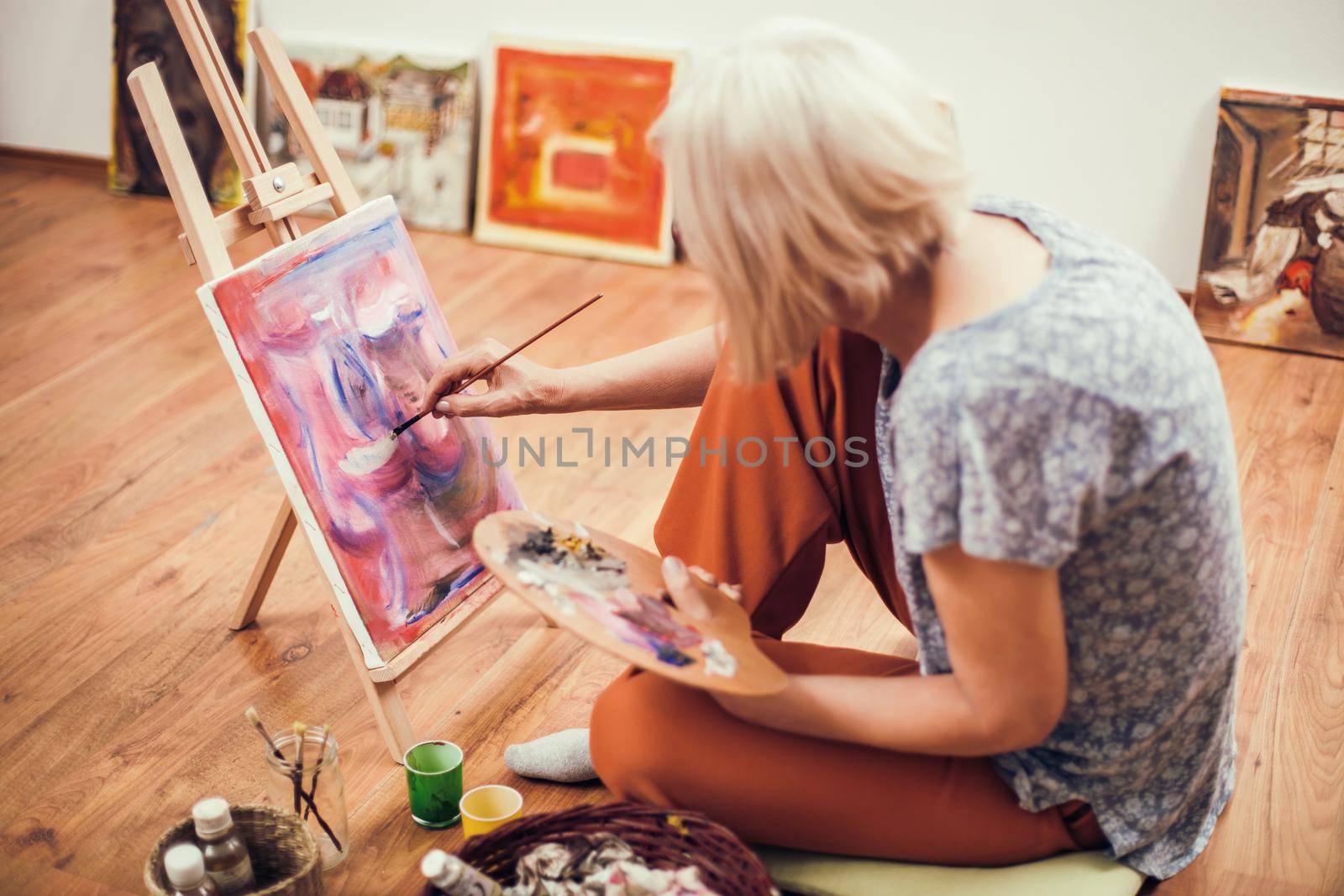 Elderly woman is painting in her home. Retirement hobby.