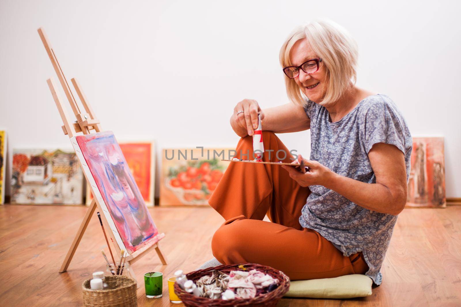 Elderly woman is painting in her home. Retirement hobby.