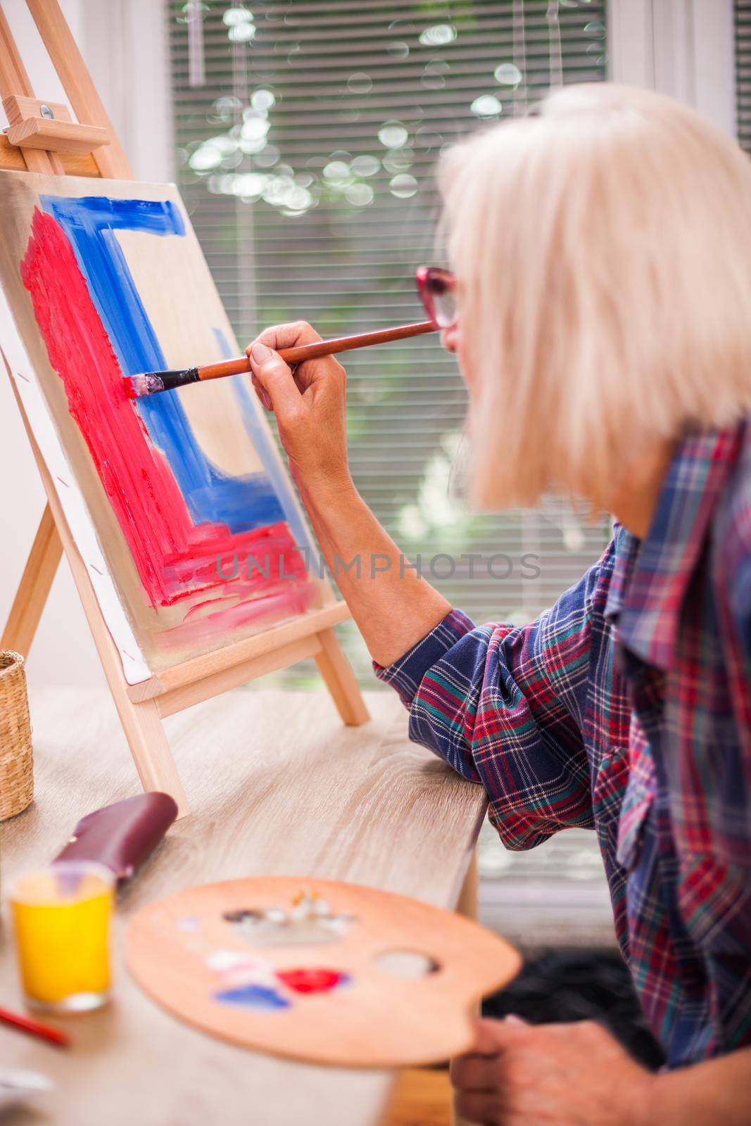 Elderly woman is painting in her home. Retirement hobby.