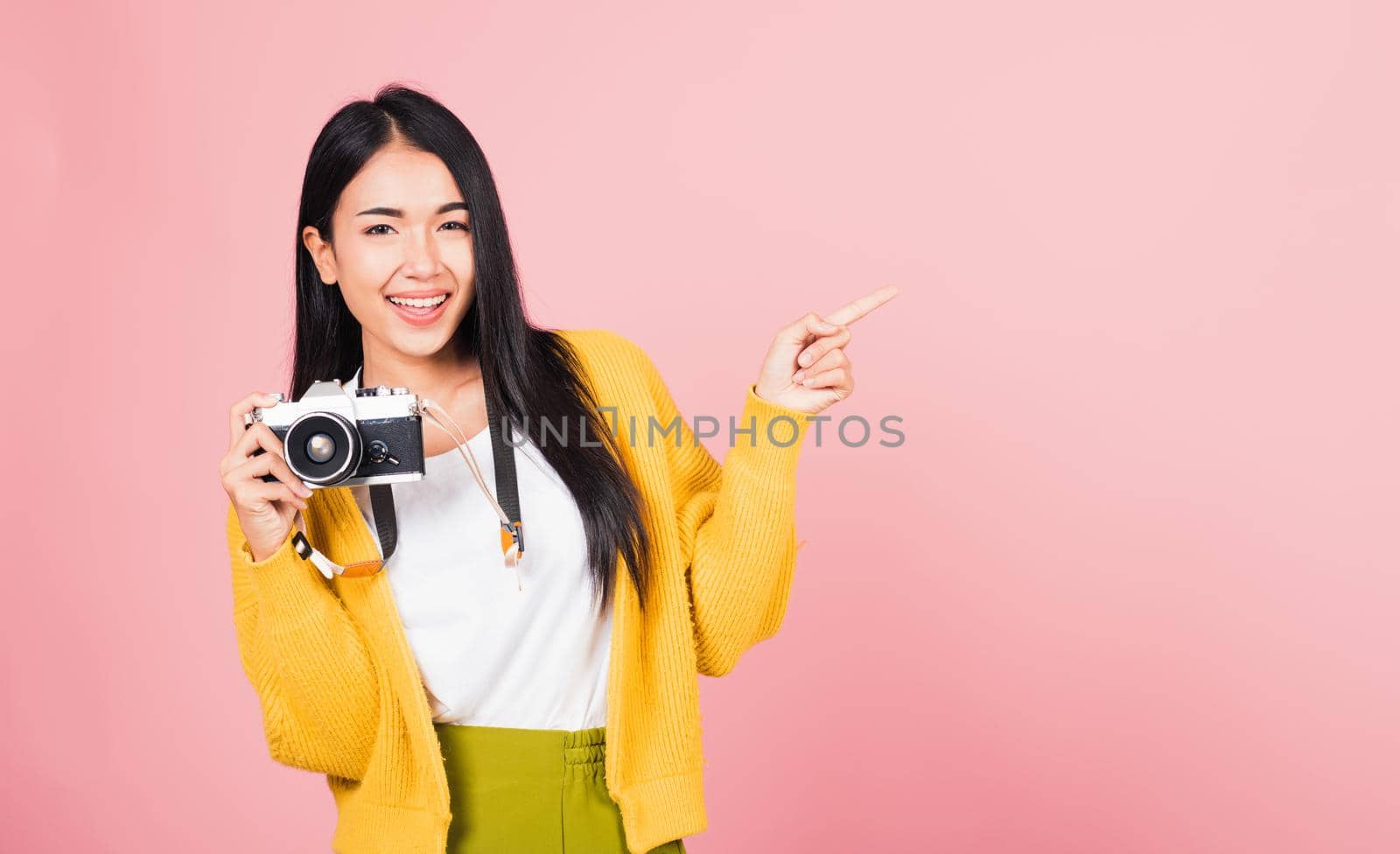 Attractive energetic happy Asian portrait beautiful cute young woman teen excited smiling holding vintage photo camera and pointing finger to side space, studio shot isolated on pink background